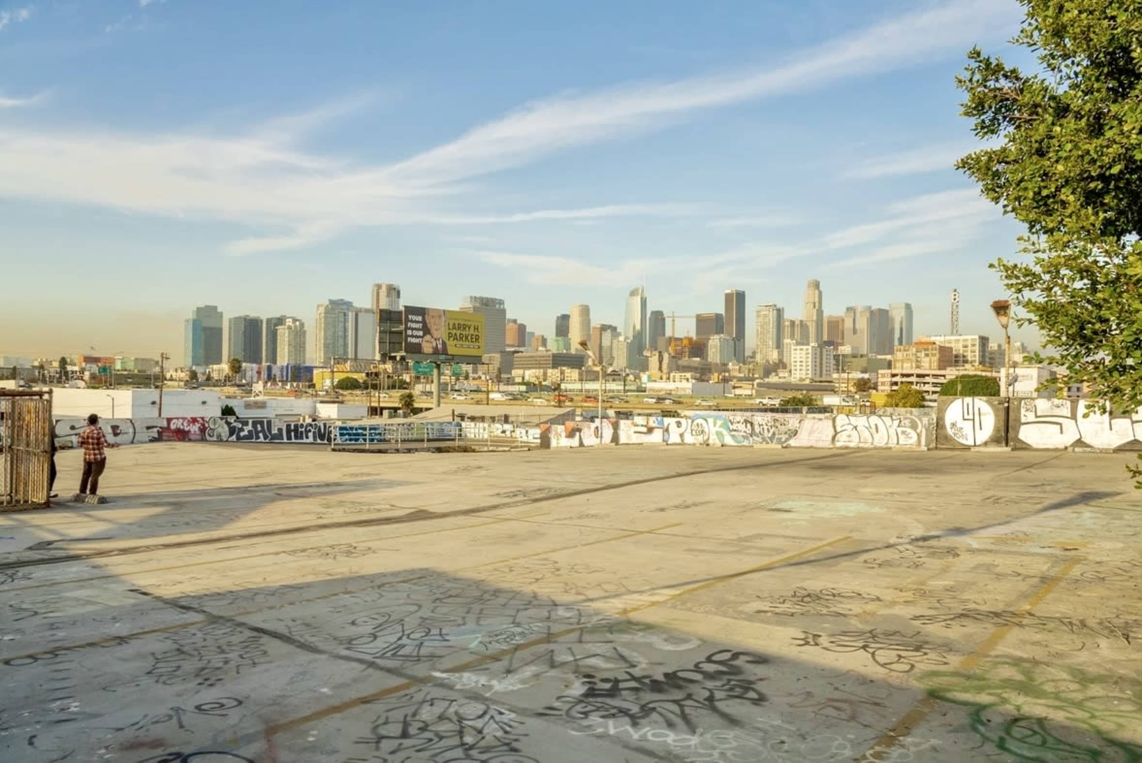 The image shows a graffiti-covered concrete area in the foreground with a view of a city skyline in the background.