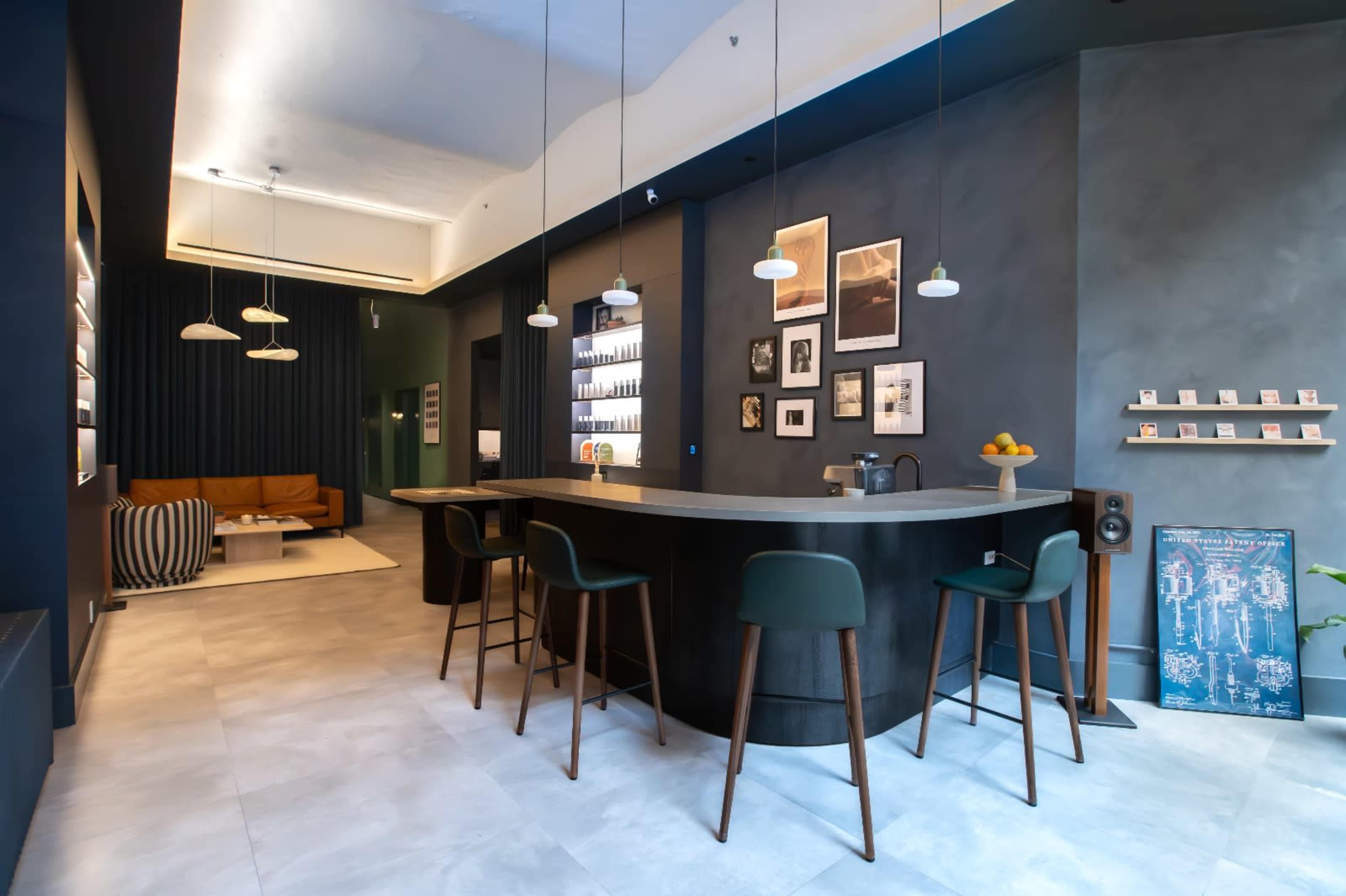 A modern interior features a curved bar with high stools, a seating area with a sofa, and newly designed walls adorned with framed photographs.