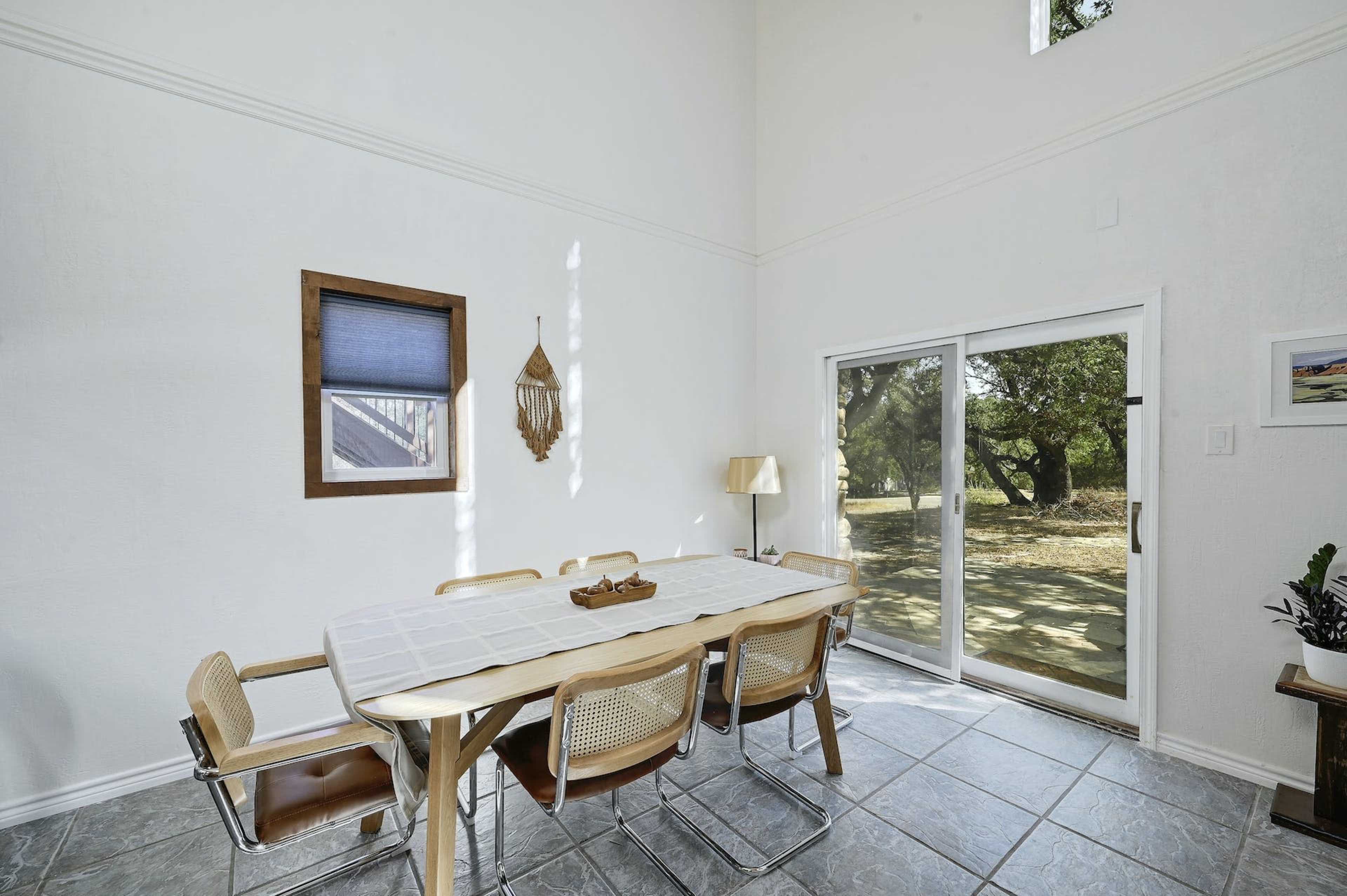 A dining area features a long wooden table surrounded by chairs, with a large glass door providing a view of the outside.