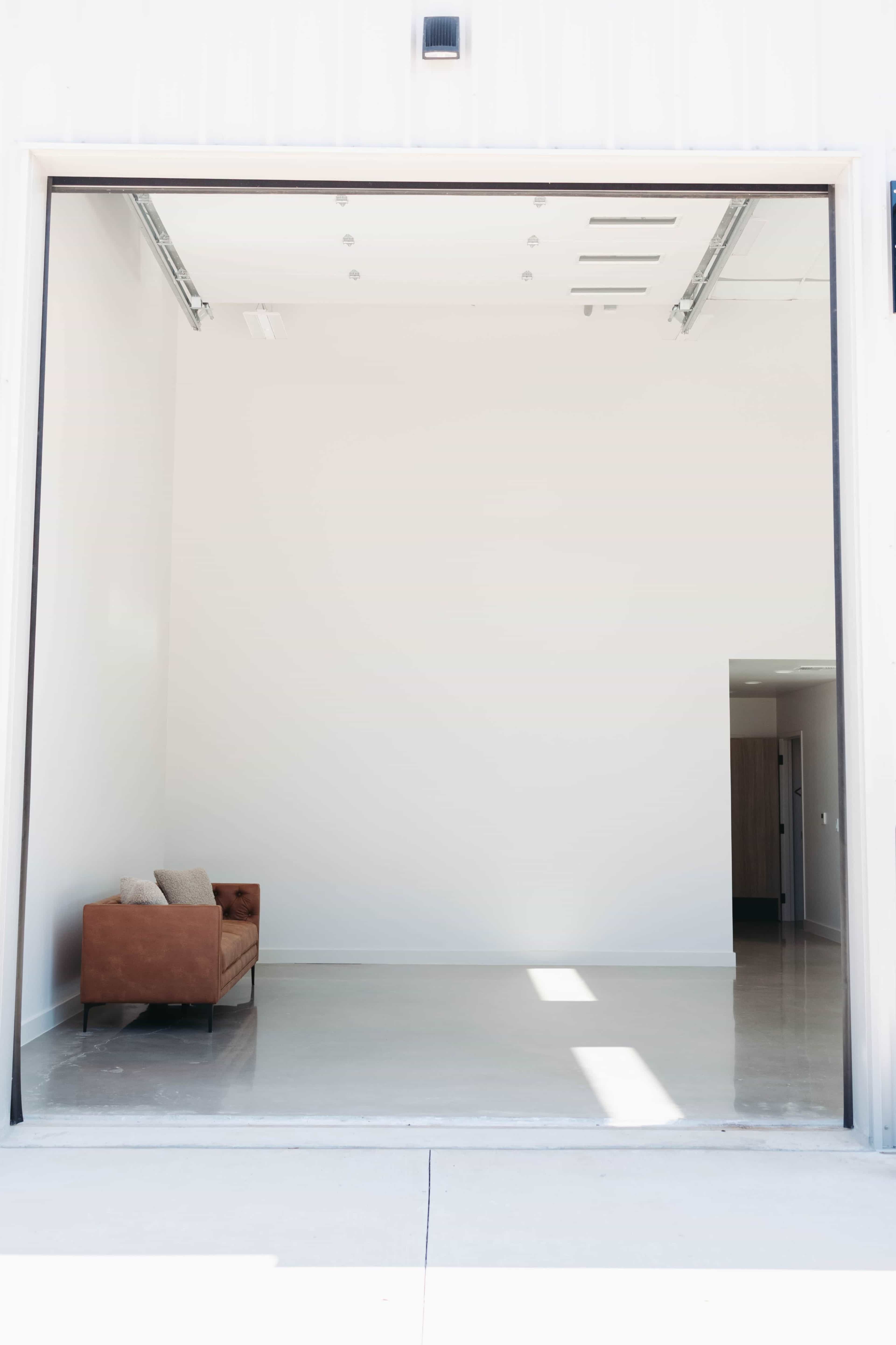 A large, empty room with white walls and a single brown couch near an open entrance.