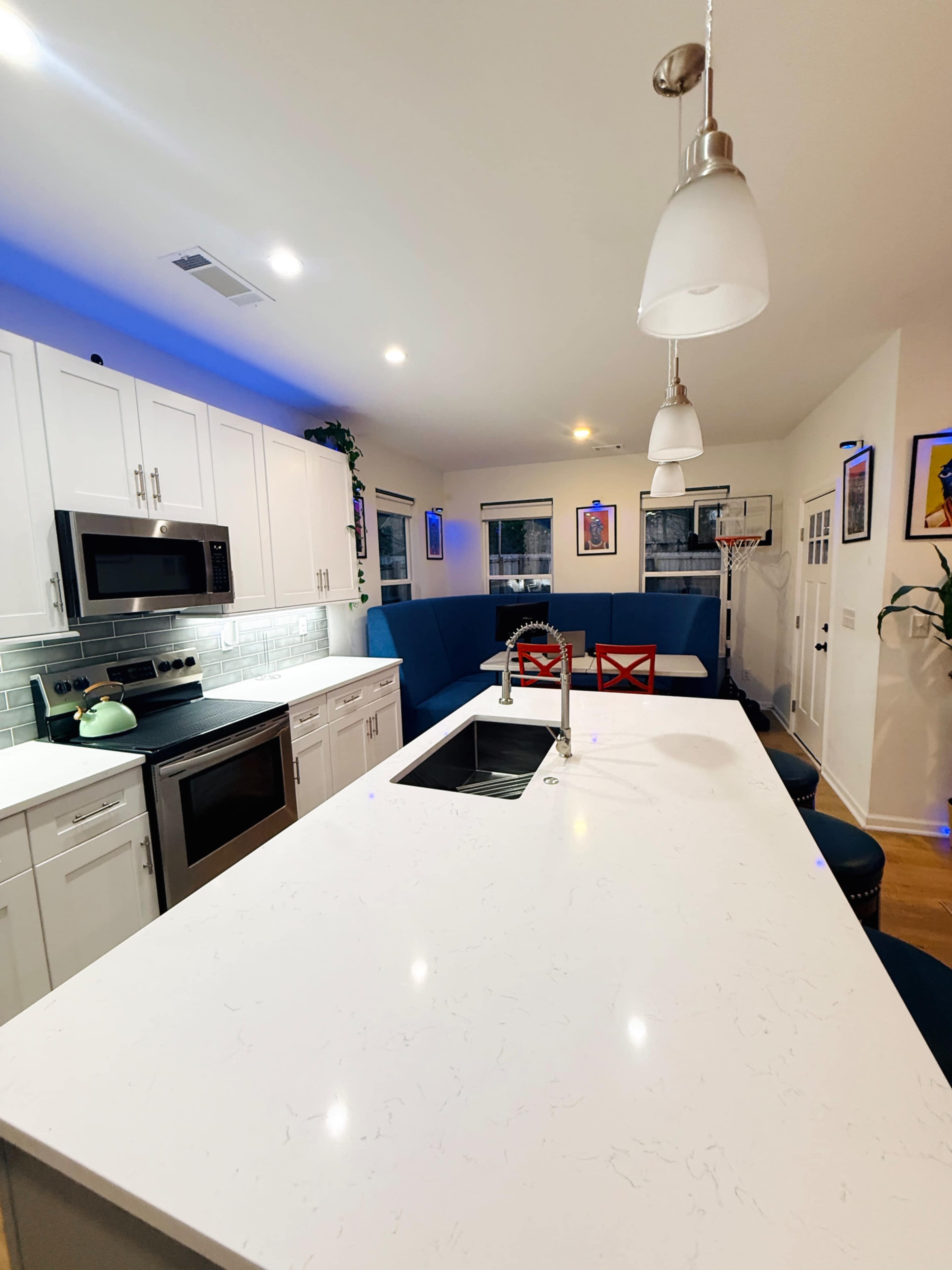 The image shows a modern kitchen with white cabinets, a large white countertop, and a blue seating area along one wall.
