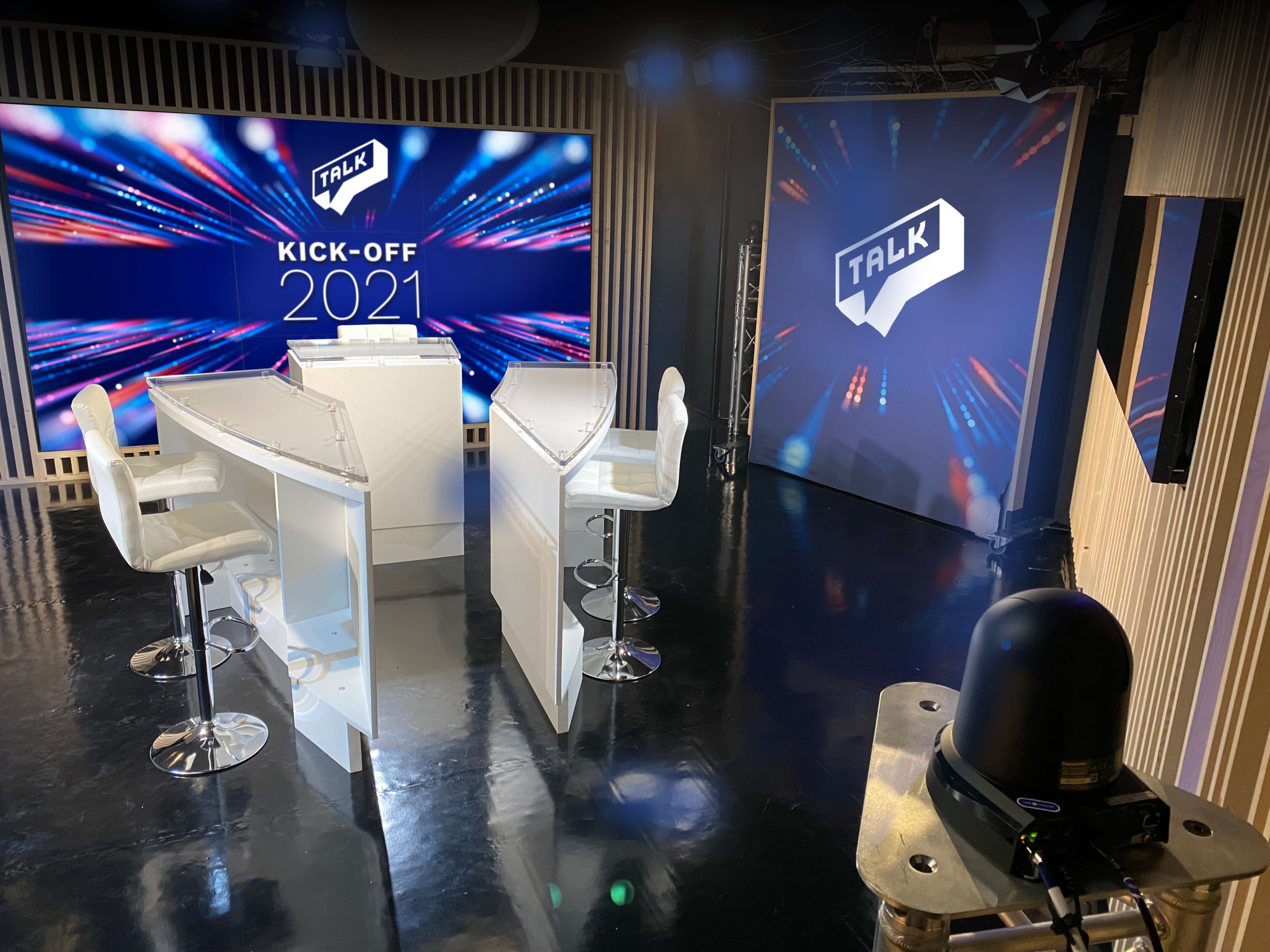 A modern studio setup with two clear podiums and a large backdrop displaying "TALK" and "KICK-OFF 2021."