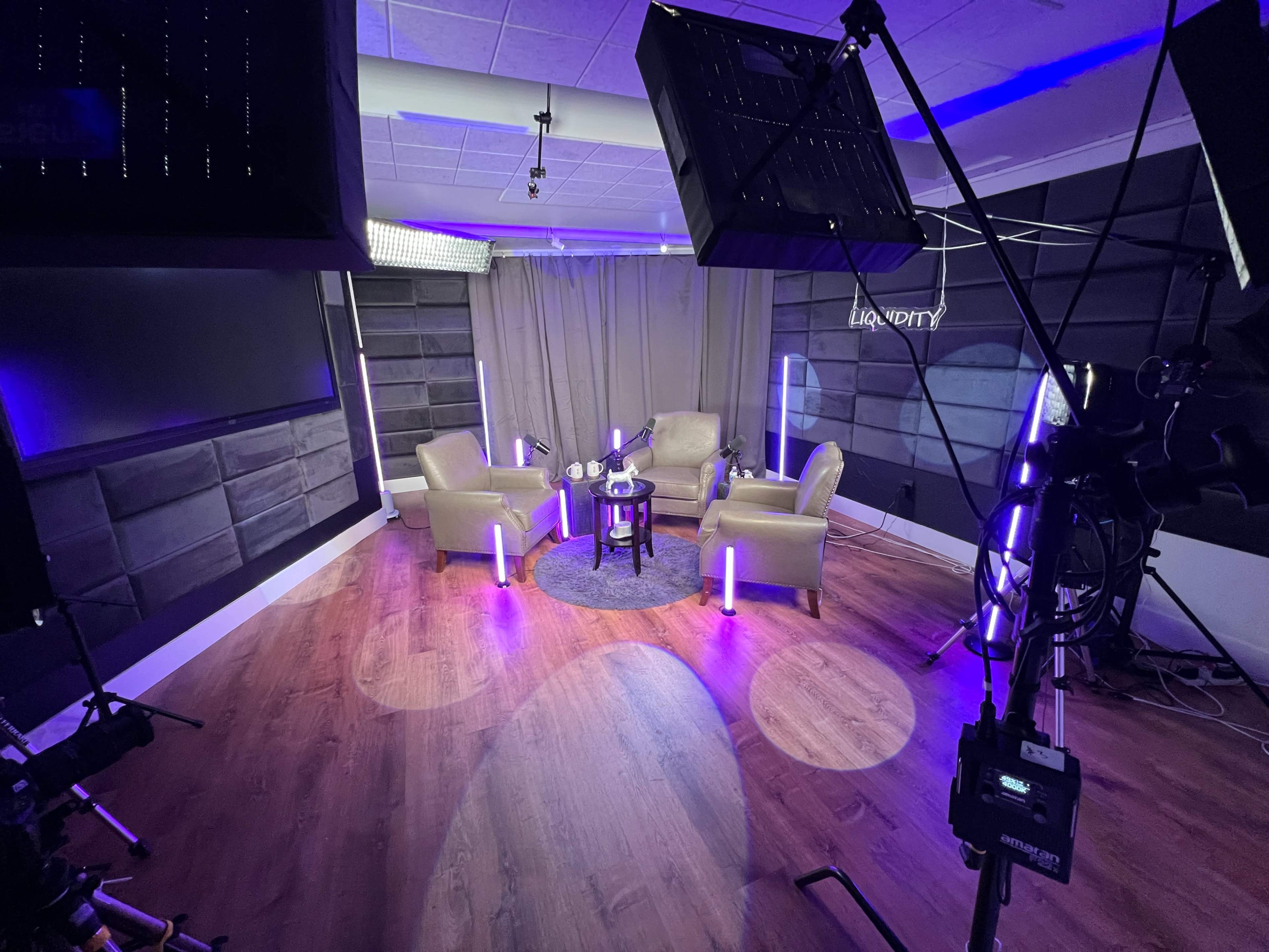 The image shows a modern studio setup with two beige chairs, a small table, and several lighting fixtures creating a vibrant atmosphere.