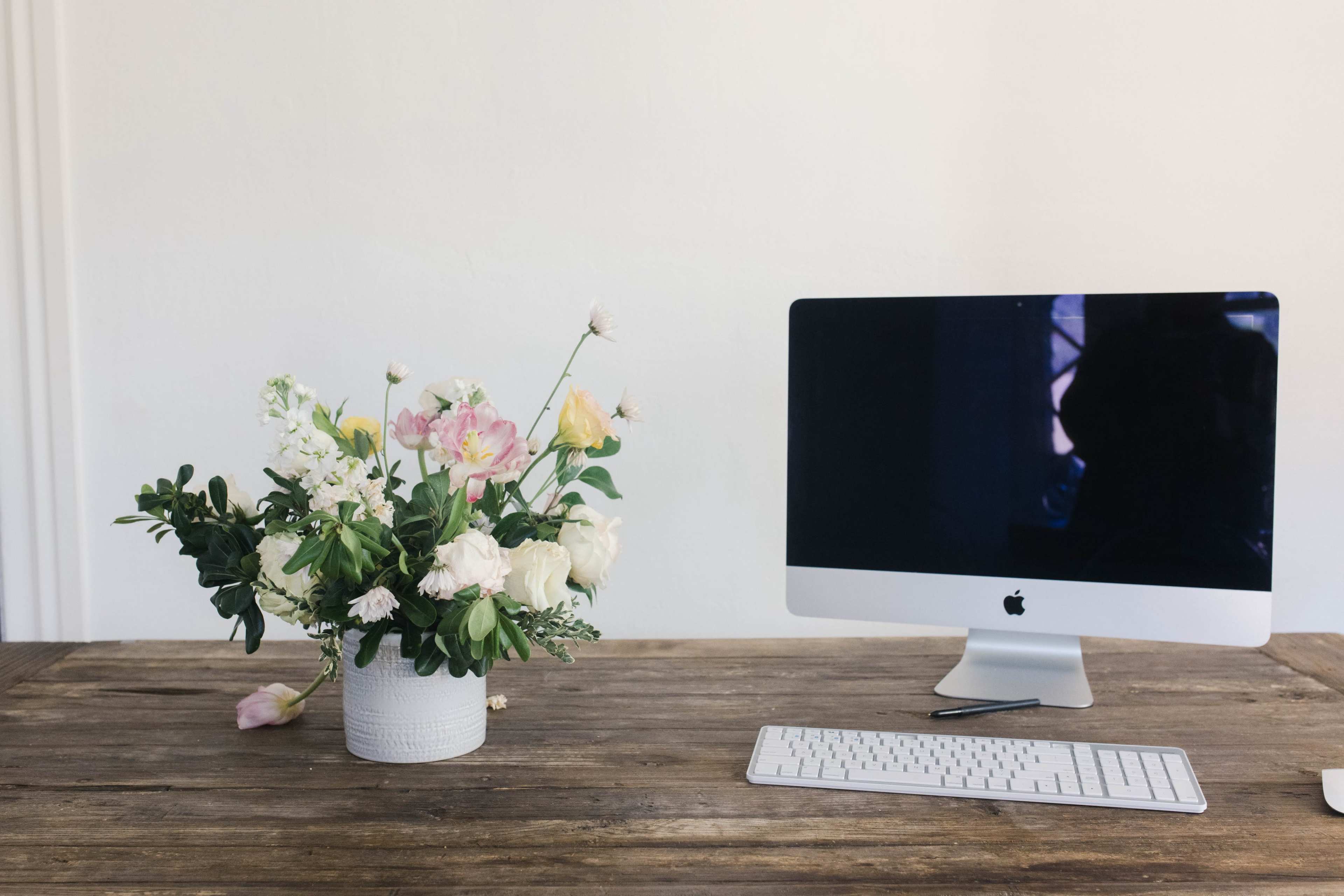 A sleek, modern computer monitor sits on a wooden desk beside a vase of fresh flowers.
