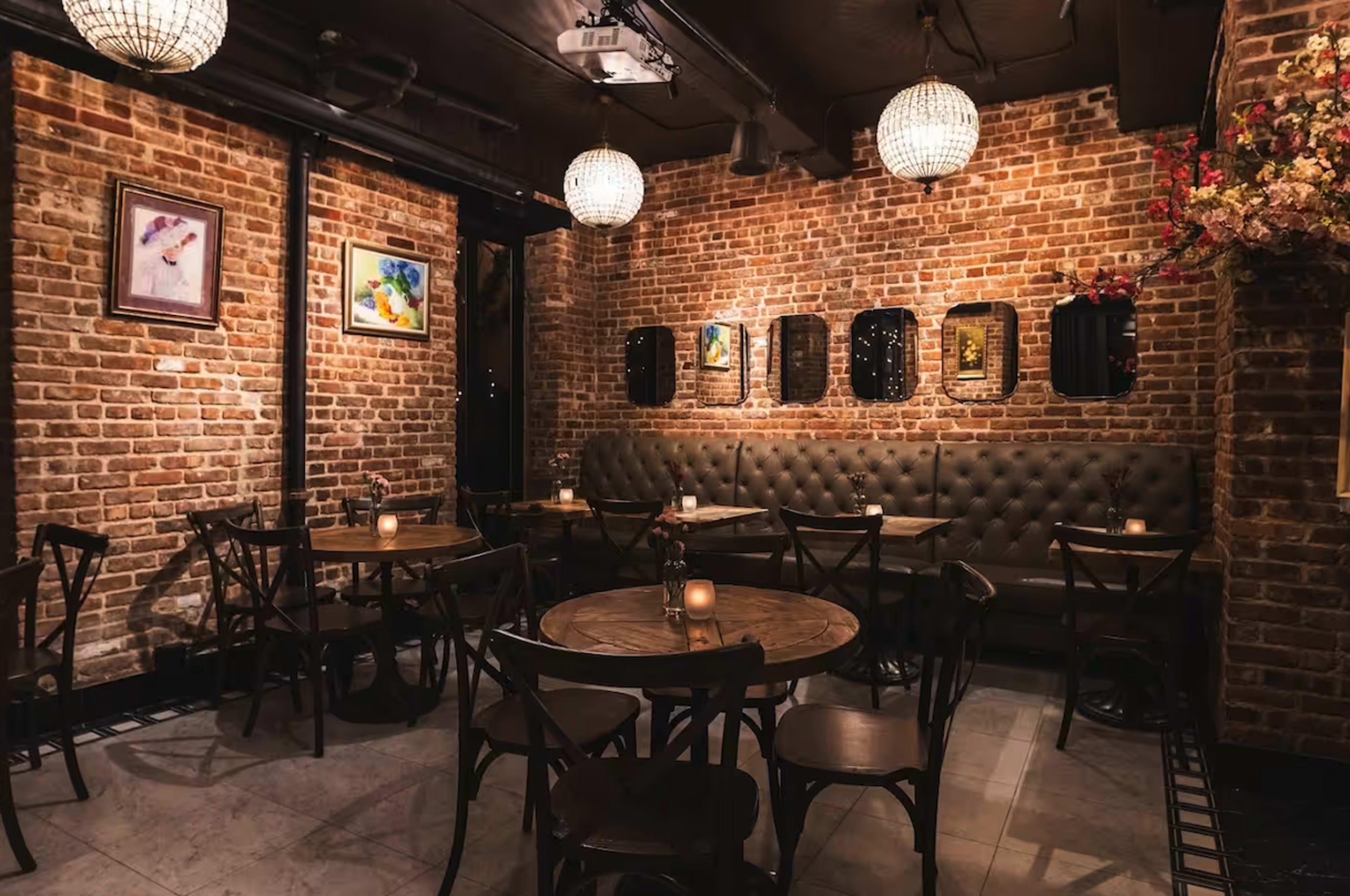 The image shows a cozy restaurant interior with exposed brick walls, wooden tables, and soft lighting from hanging chandeliers.