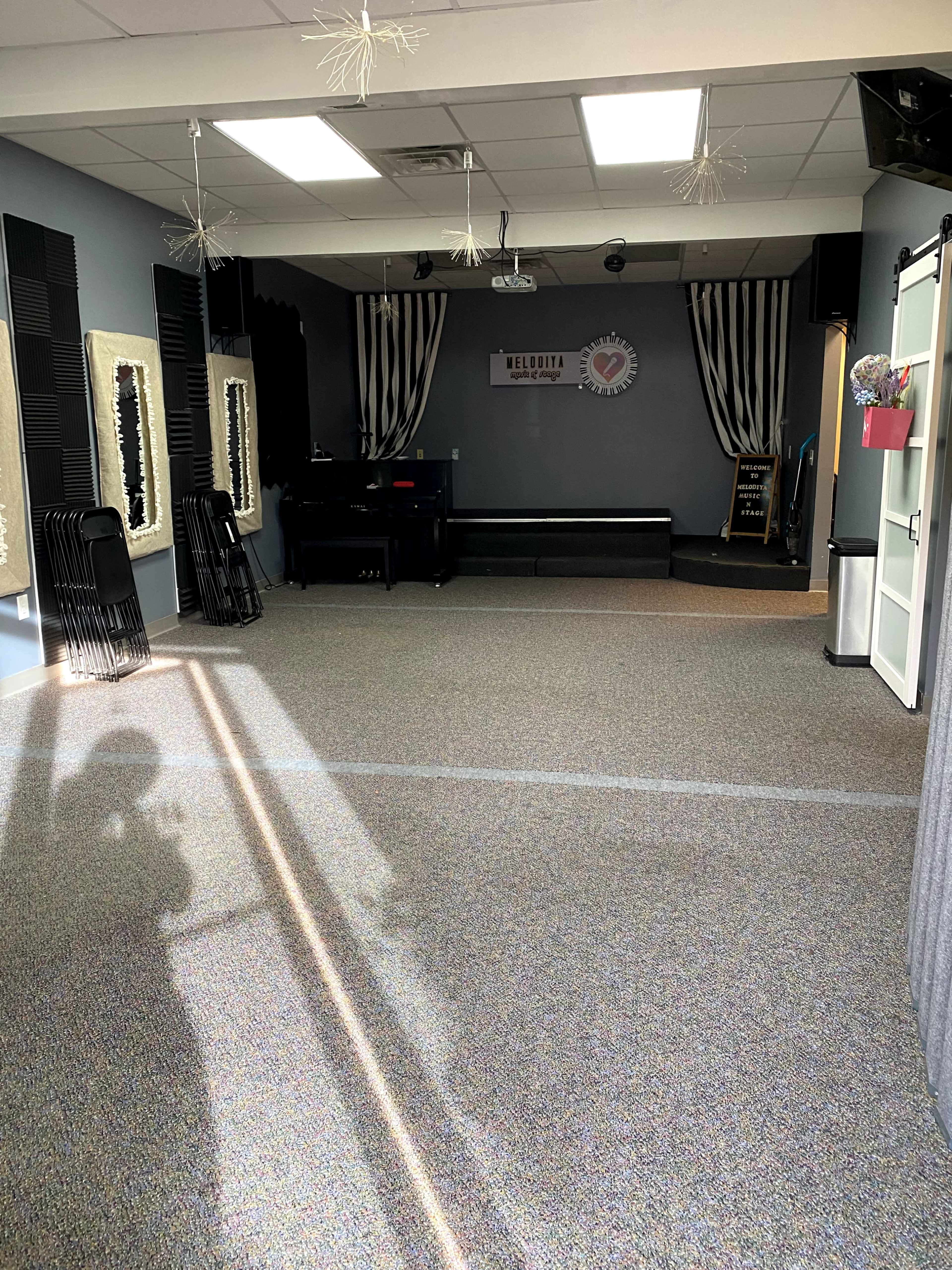 An empty rehearsal space with a piano, stage area, and decorative curtains against the walls.