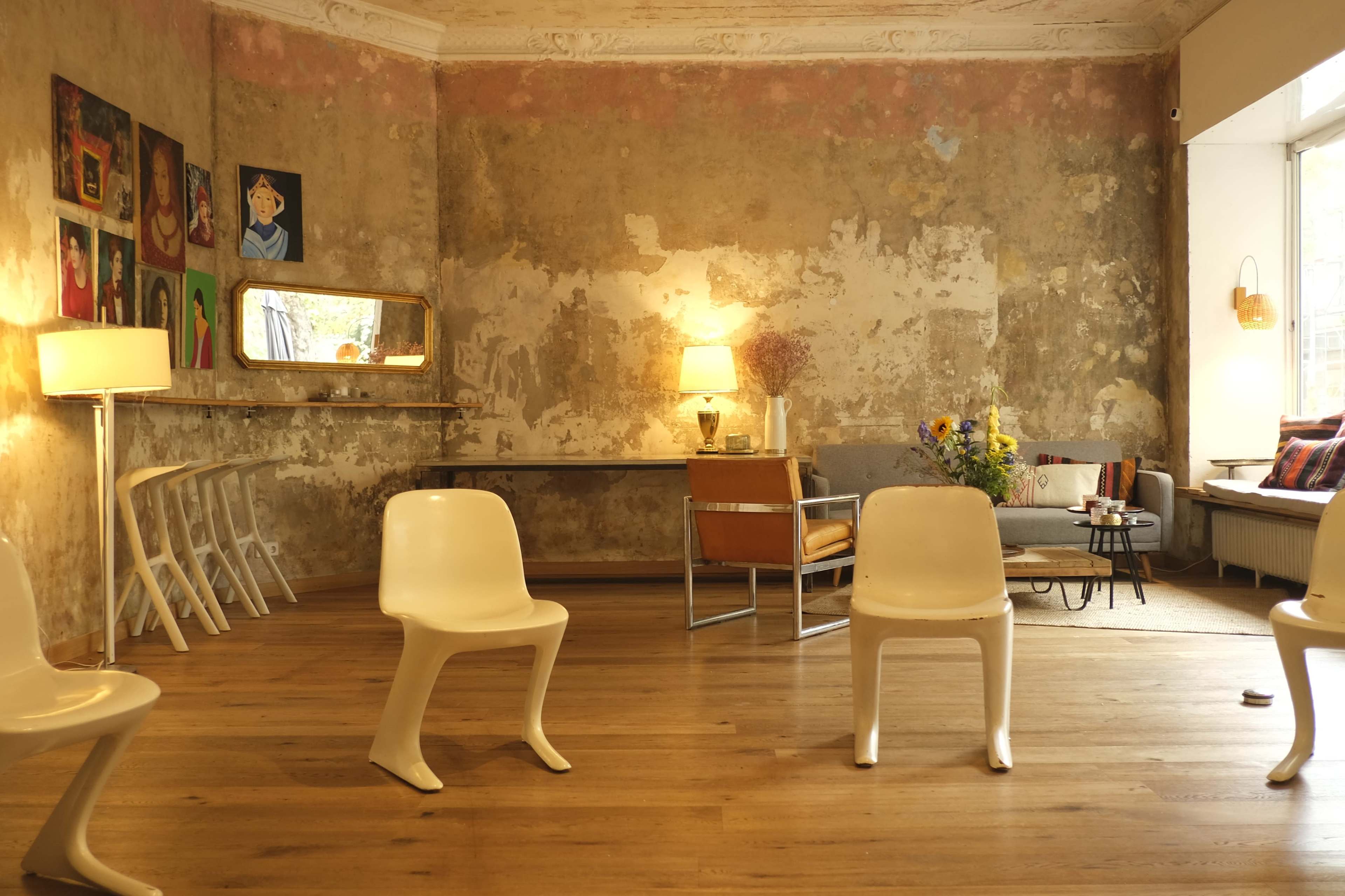 A sparsely furnished room features a mix of modern chairs, a table, artwork on the walls, and a bright window.