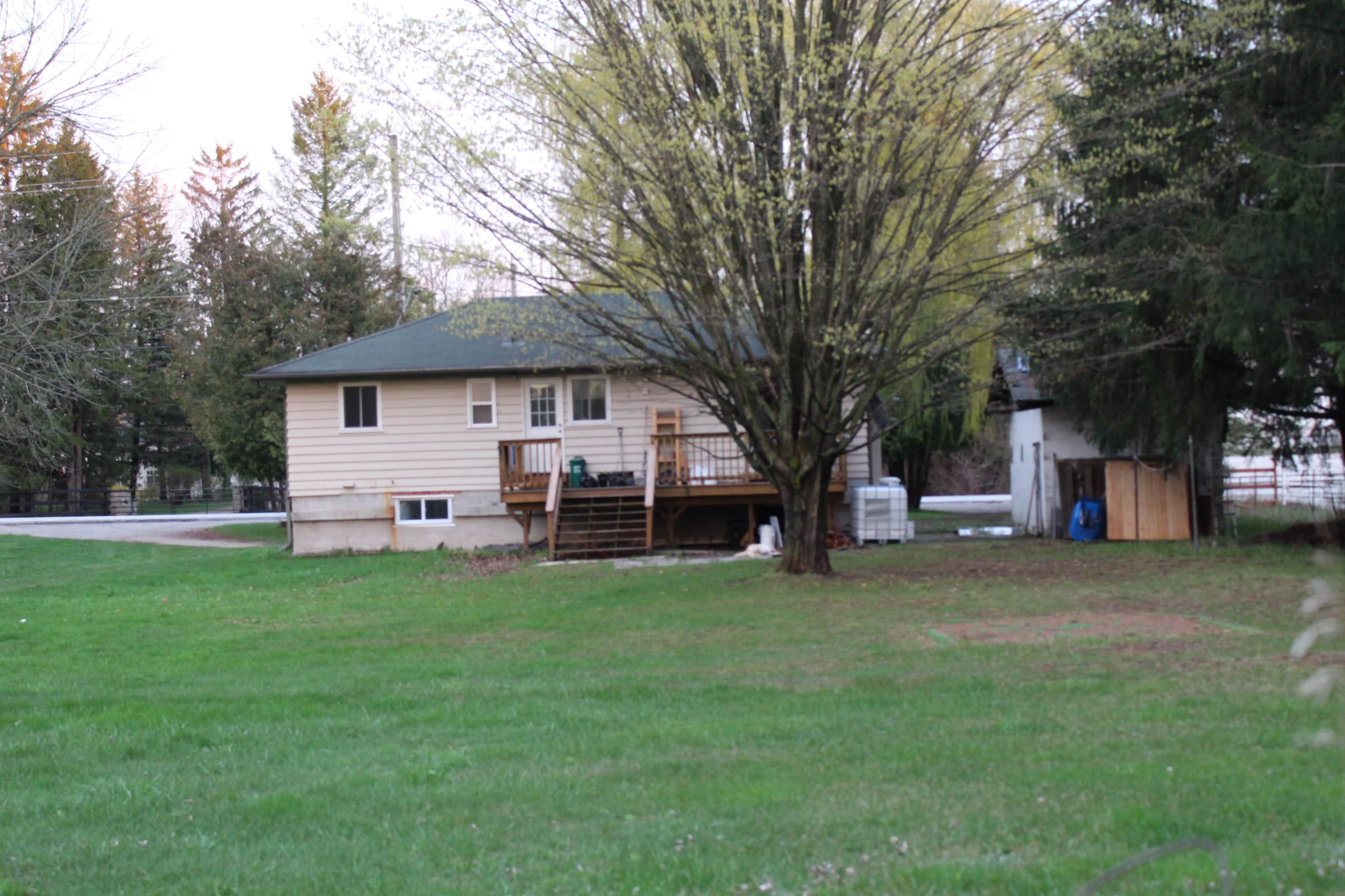 A single-story house with a front porch, surrounded by trees and a grassy yard.