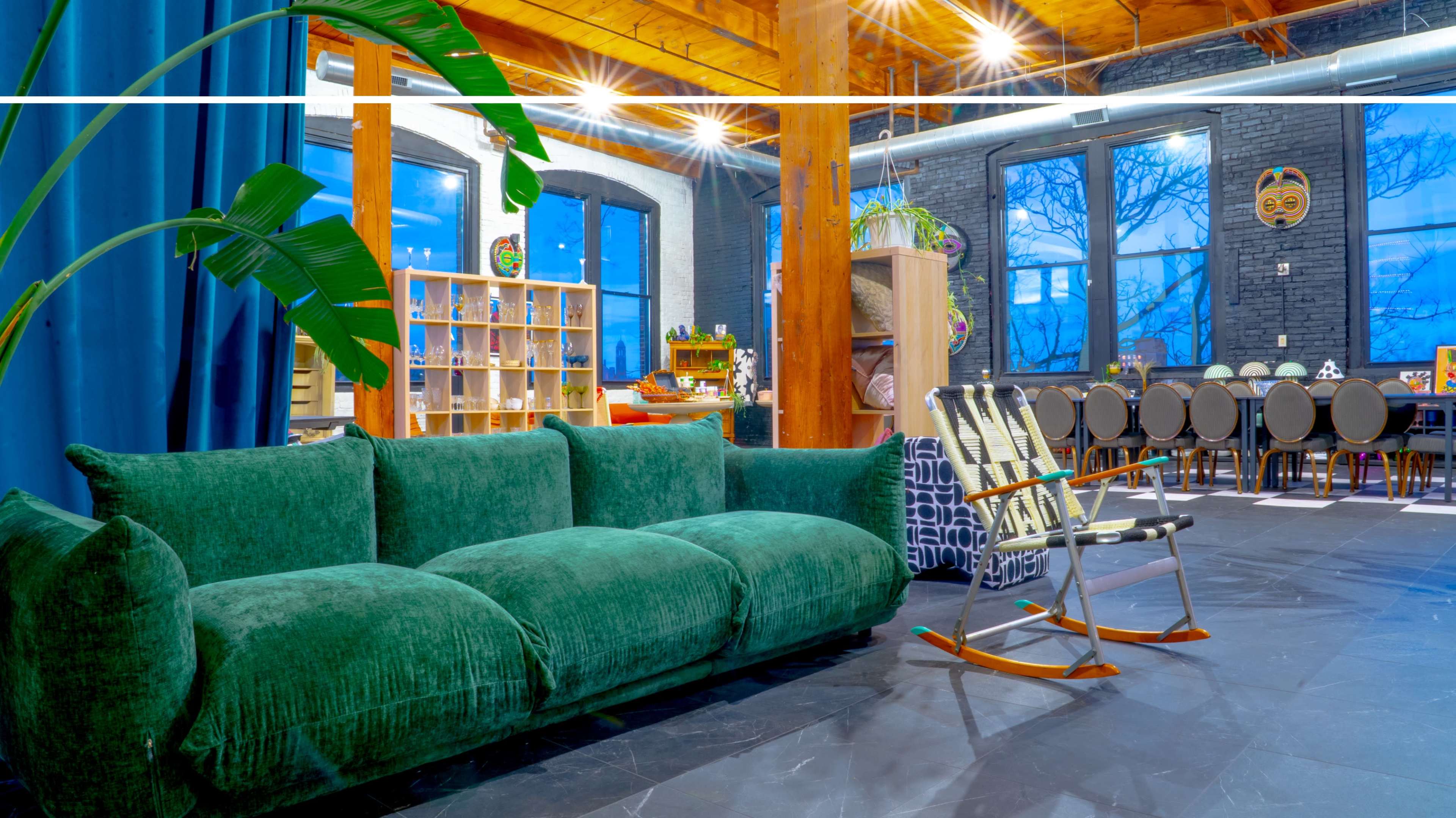 The image shows a modern interior space featuring a green sofa, large windows, and a mix of seating options arranged around a central table.