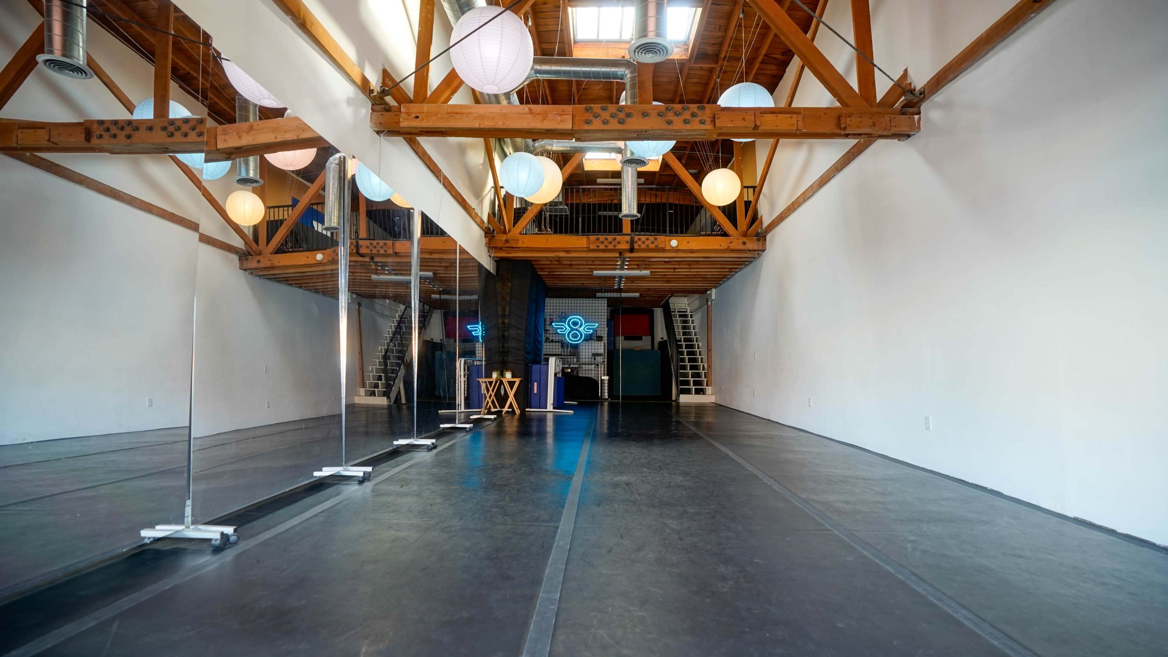 A spacious dance studio with wooden beams, large mirrors, and decorative paper lanterns hanging from the ceiling.