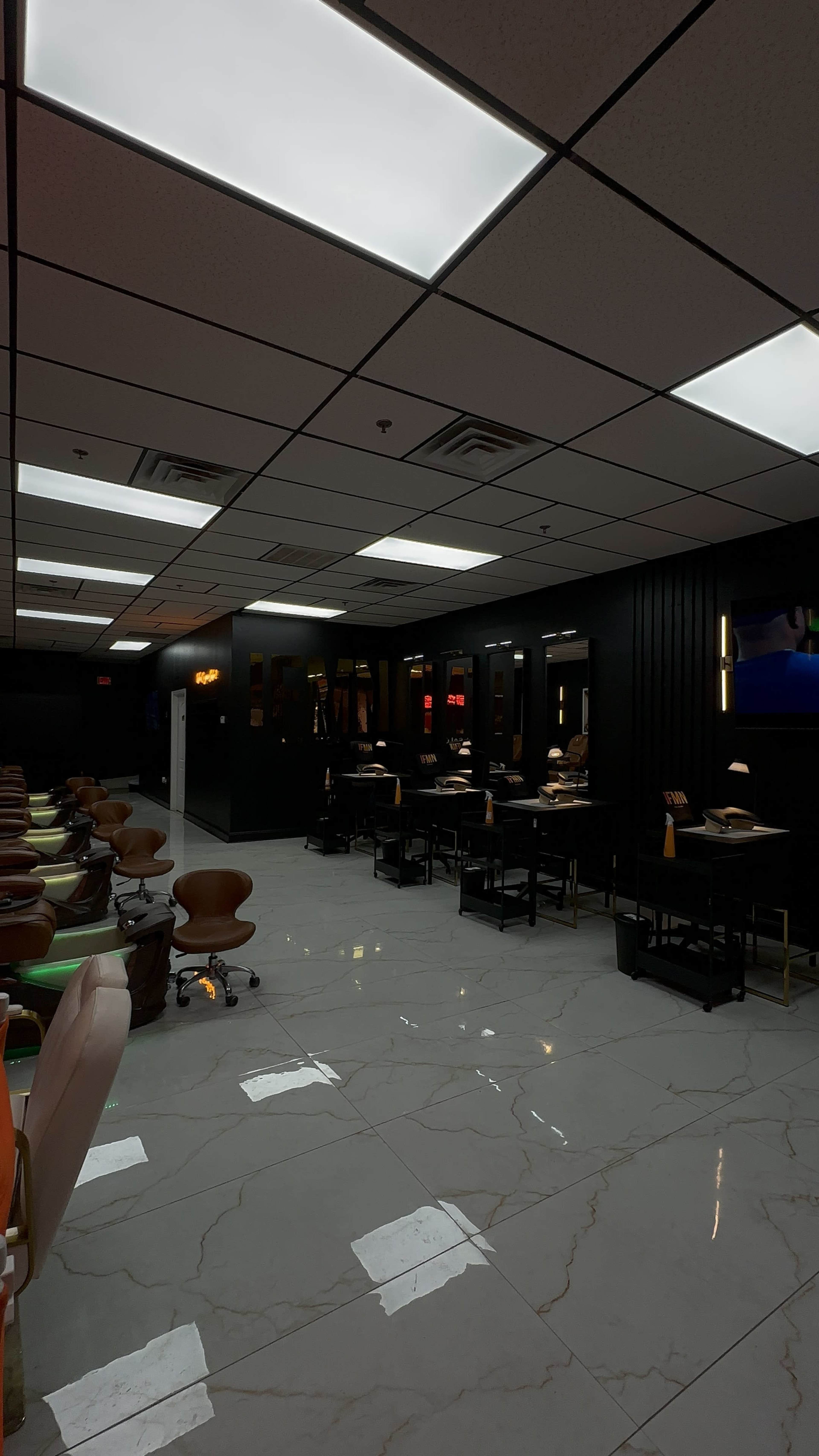 The image shows the interior of a nail salon with multiple manicure stations and plush seating arranged in a spacious layout.