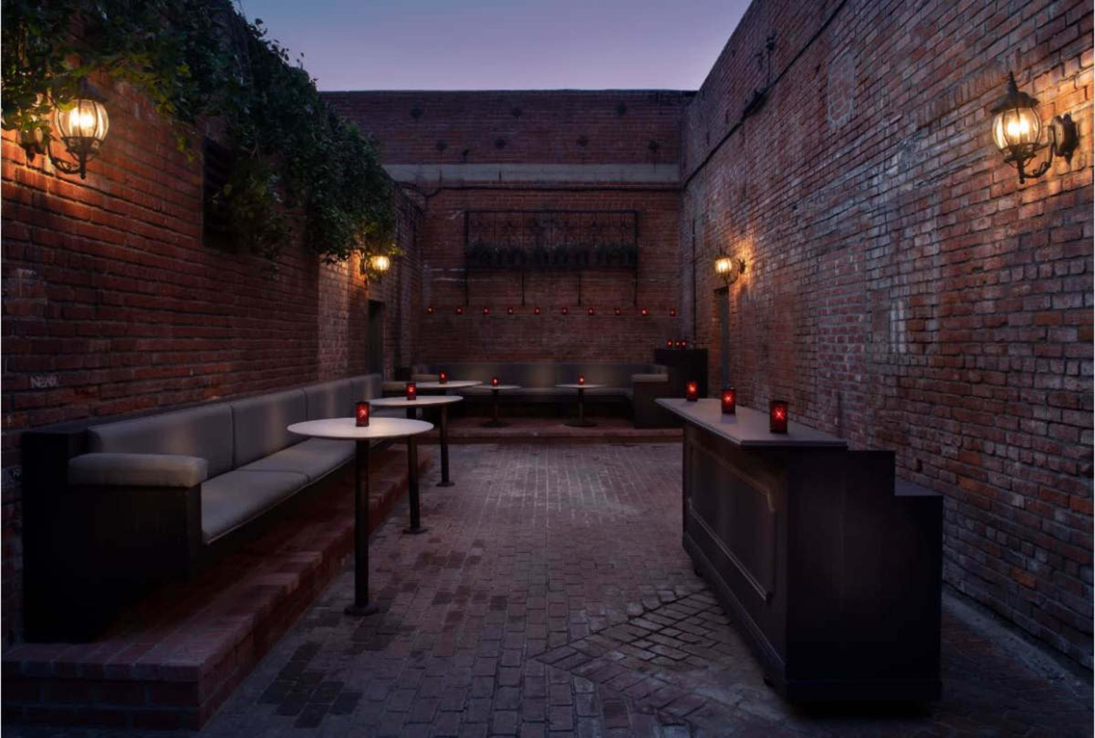 The image shows a brick-walled outdoor bar area with soft seating, ambient lighting, and small tables.