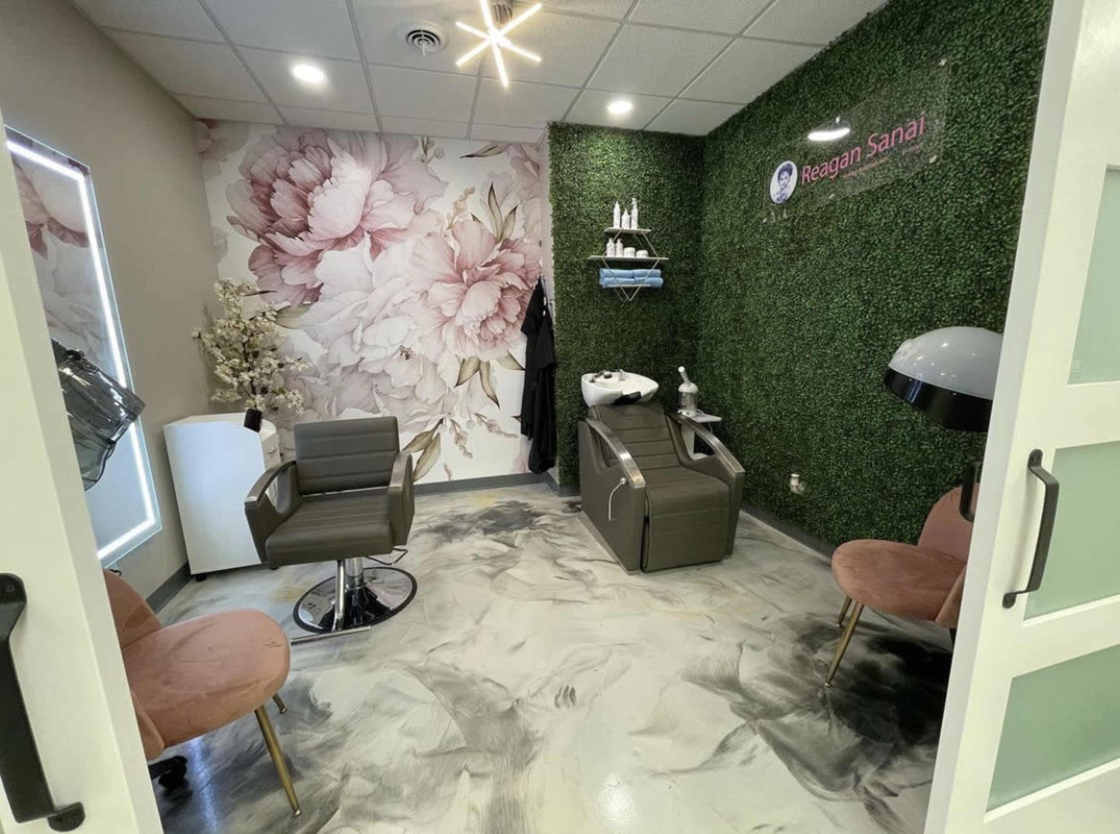 A small salon room with two pink chairs, a shampoo station, and a green wall adorned with floral wallpaper.