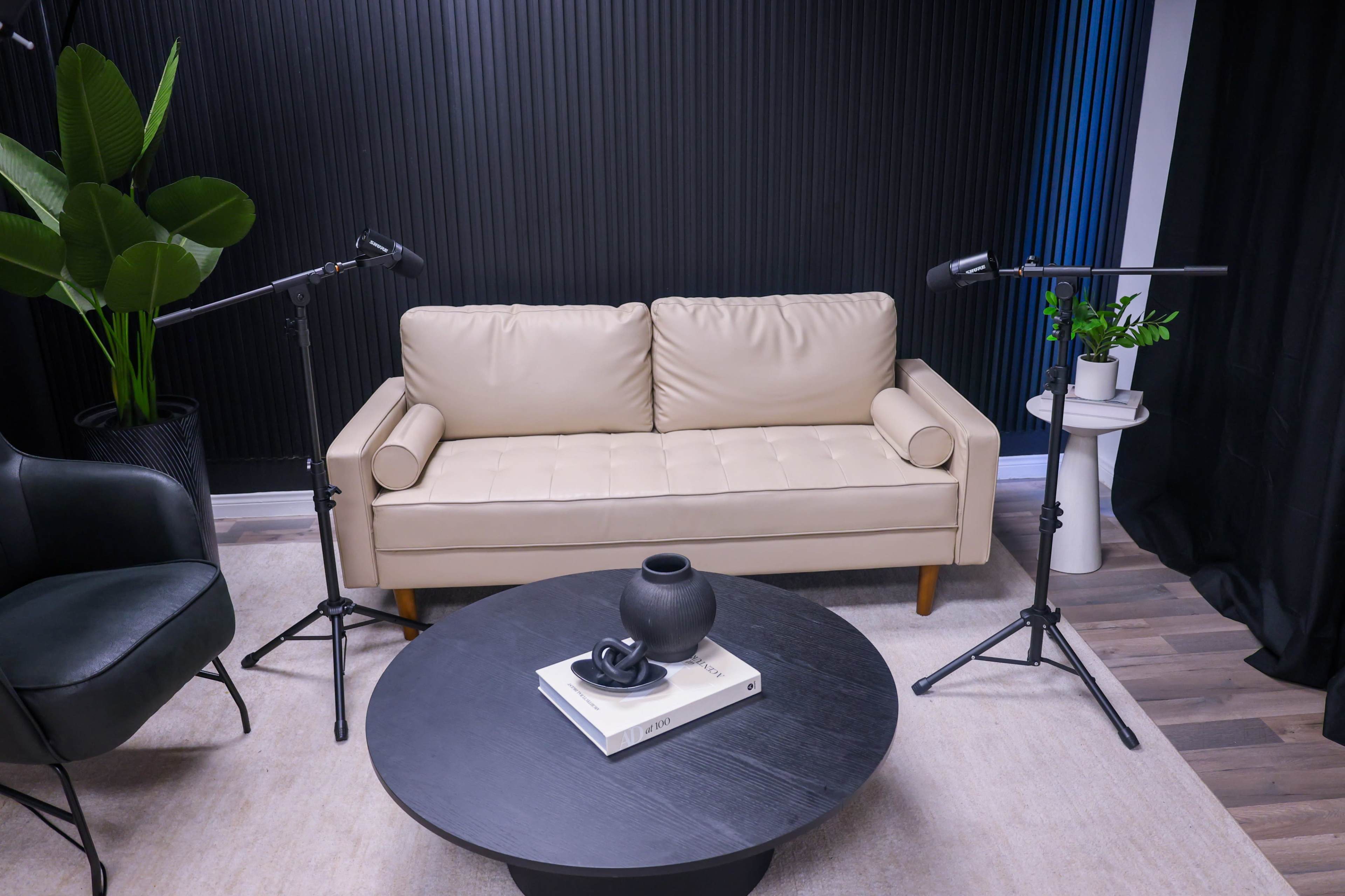 The image shows a modern living room setup featuring a light-colored sofa, a round black coffee table with decor, and two microphones on stands.