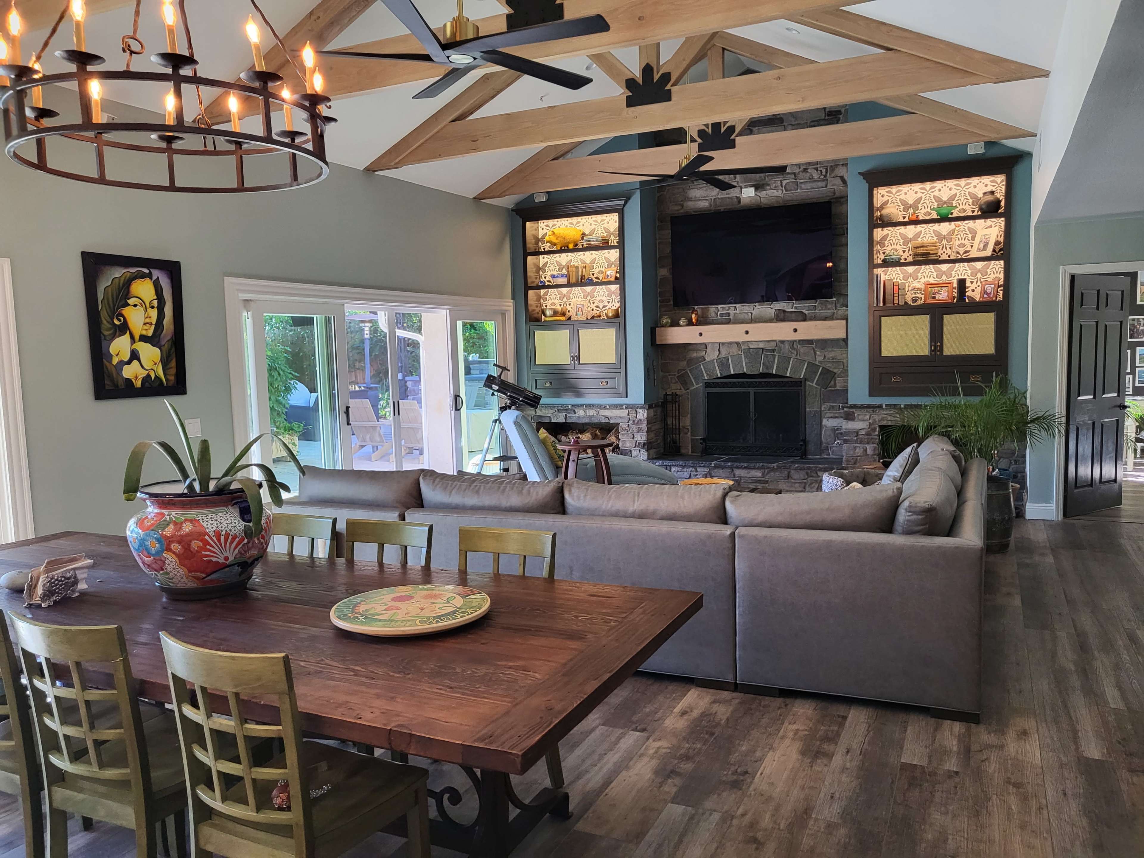 A spacious living room with a stone fireplace, a large sectional sofa, a wooden dining table, and decorative built-in shelves.