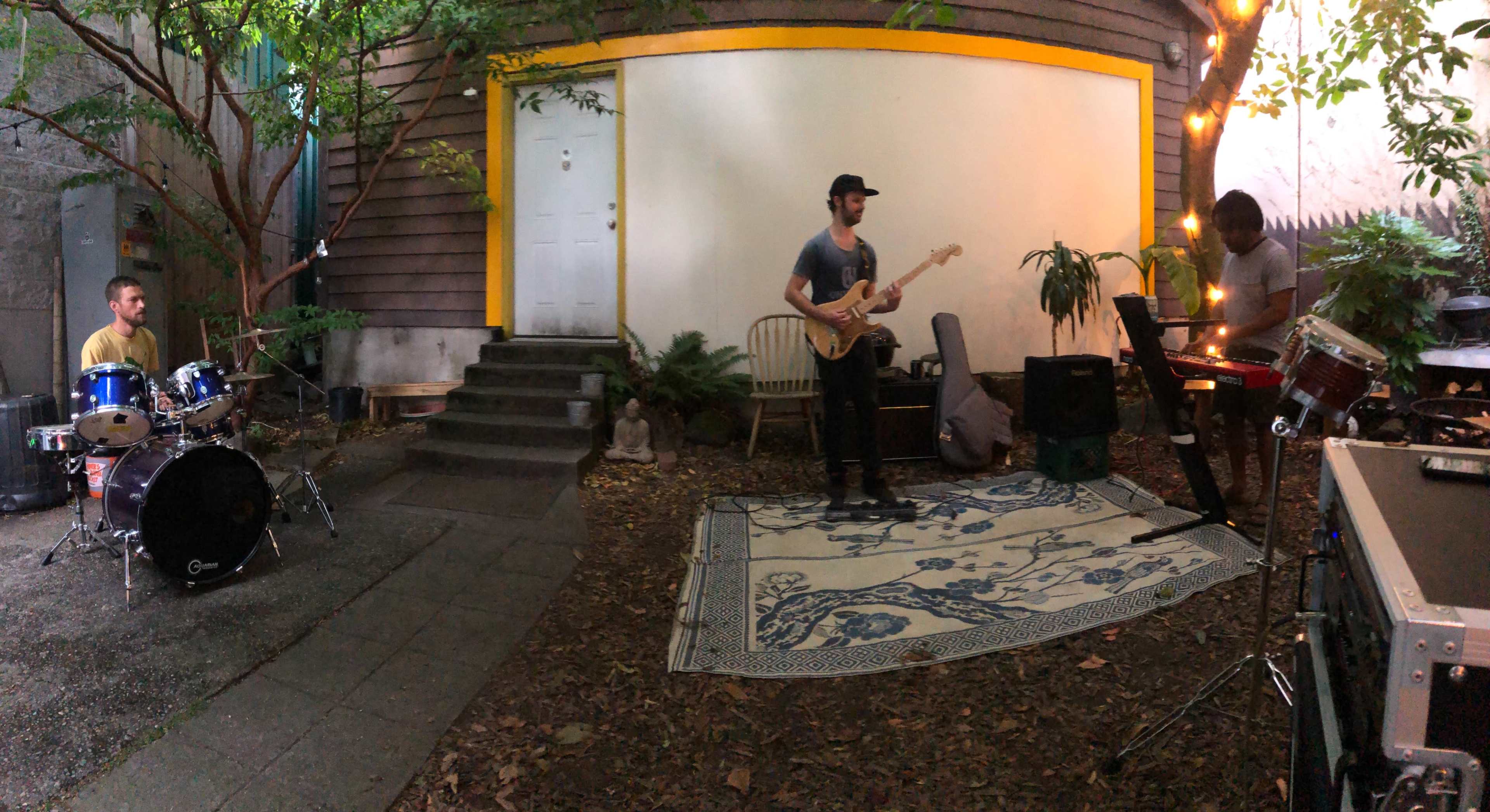 A band performs in a cozy outdoor space surrounded by greenery and string lights.