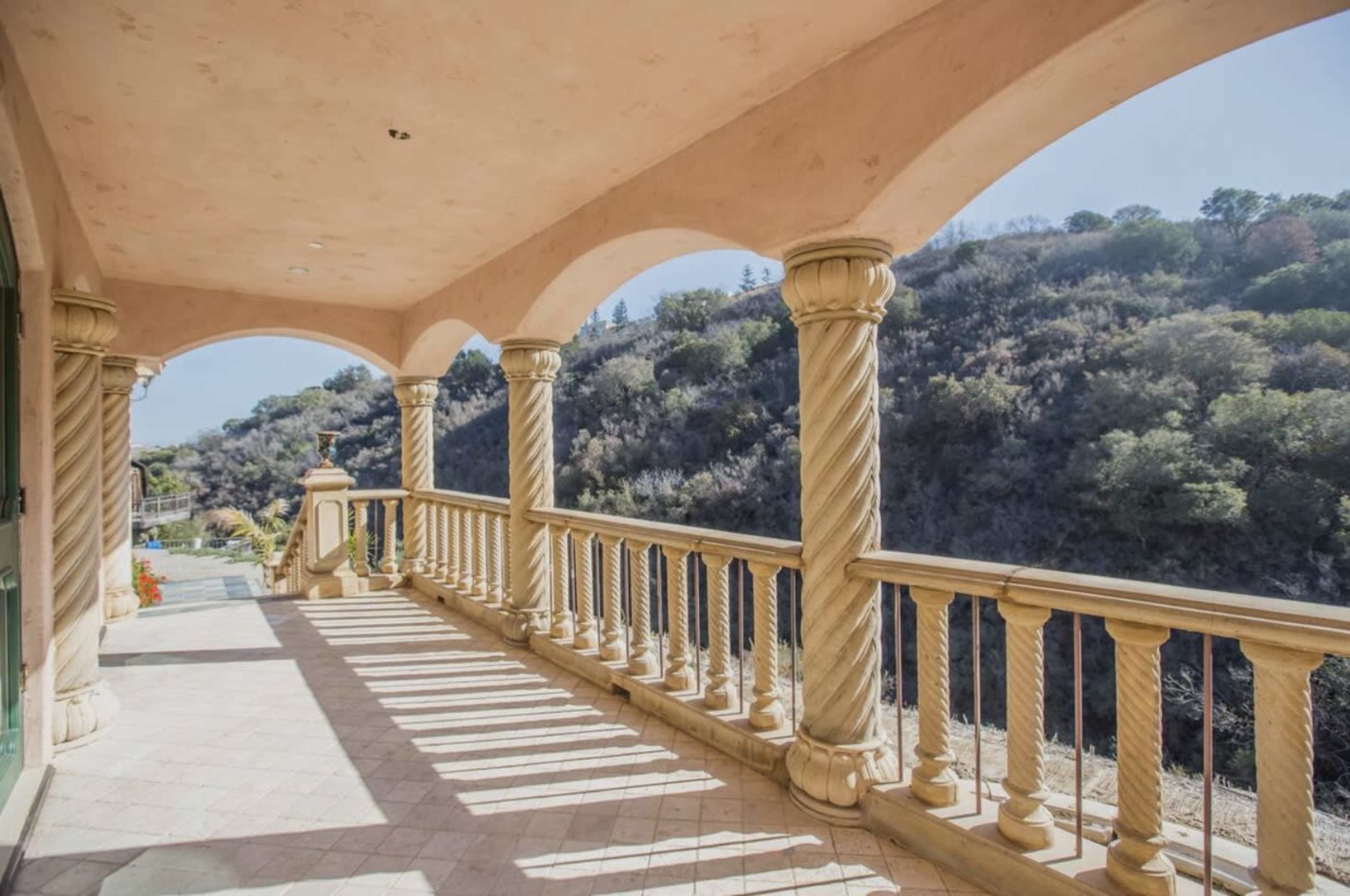A landscaped balcony with decorative columns overlooking a hilly terrain.