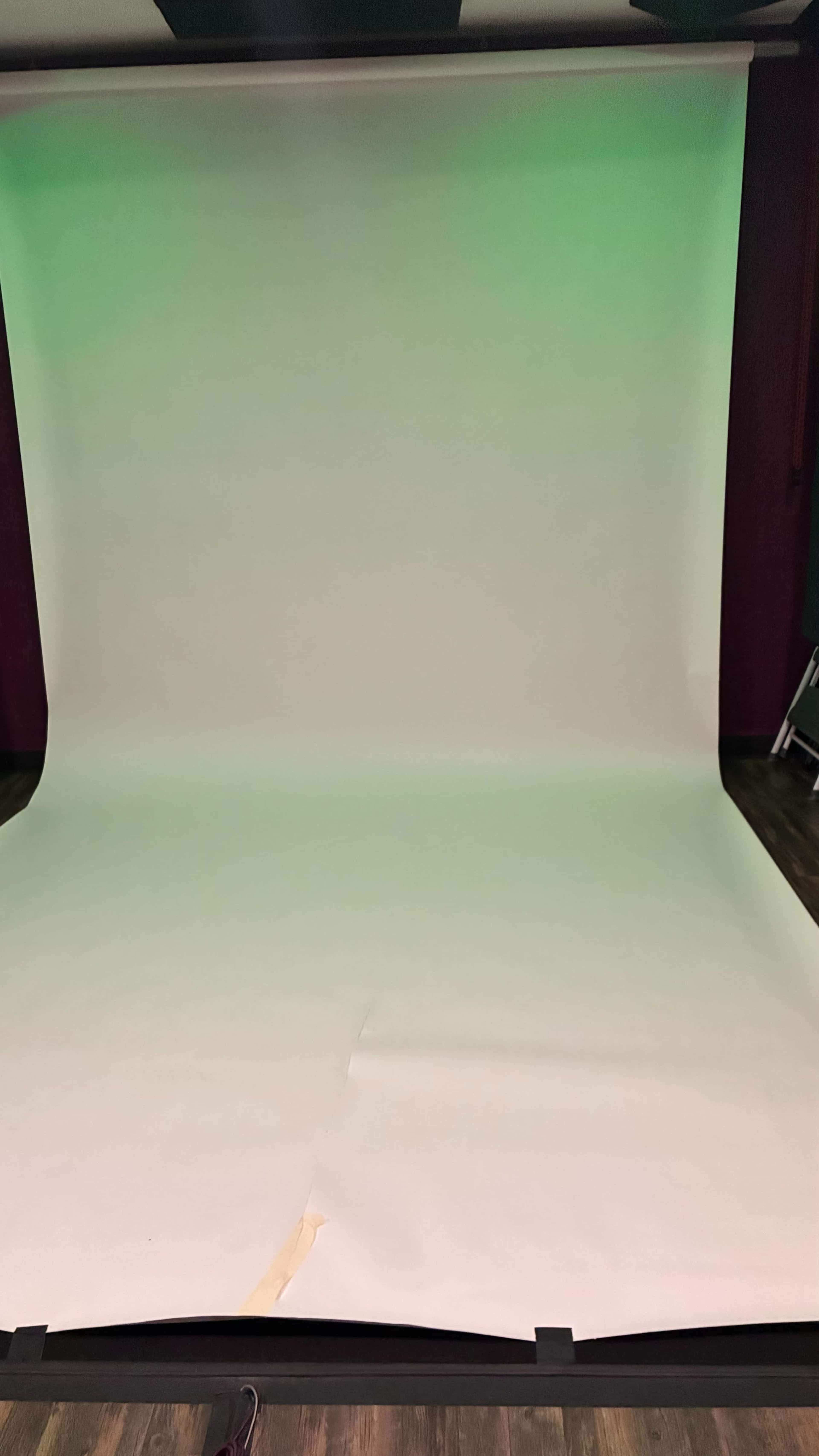 The image shows a blank photography backdrop with a smooth white surface and a green gradient at the top.