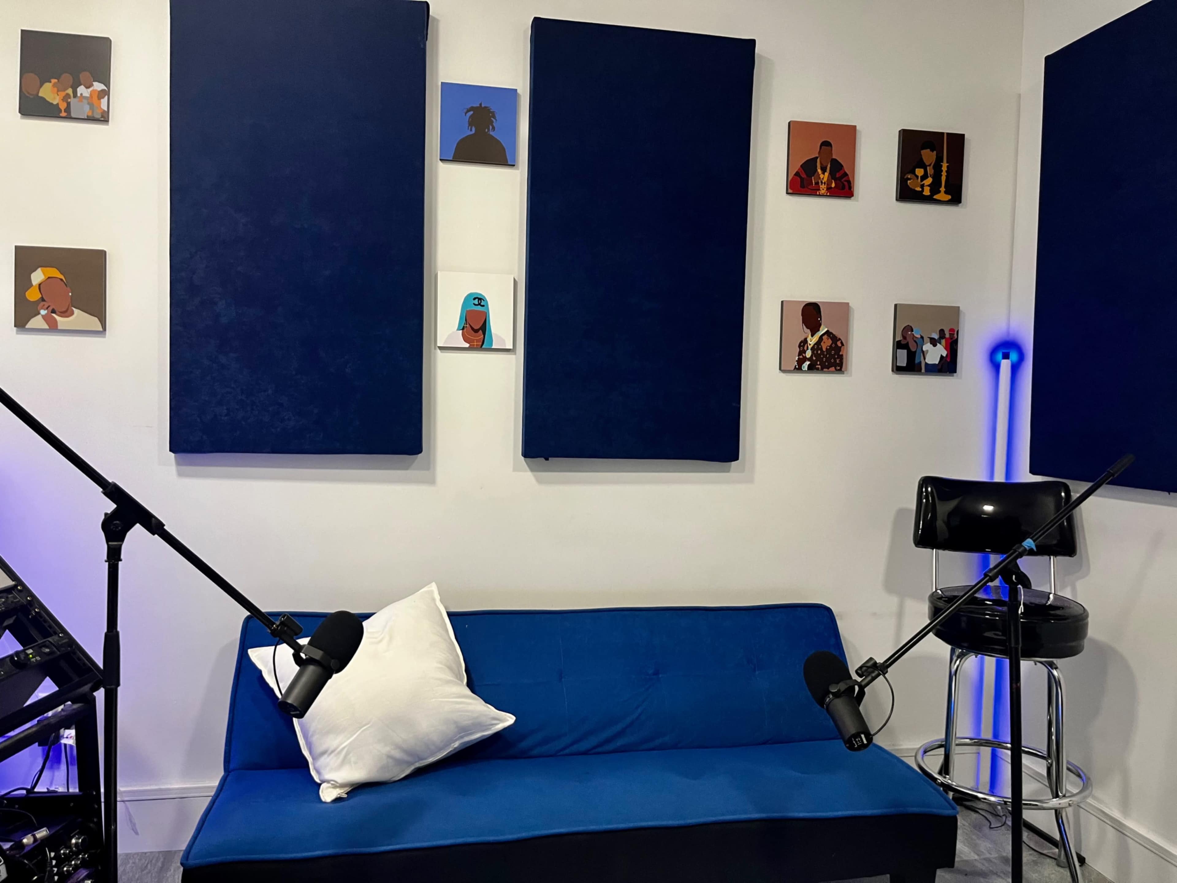 A recording studio with a blue couch, two microphones on stands, and artwork mounted on the walls.