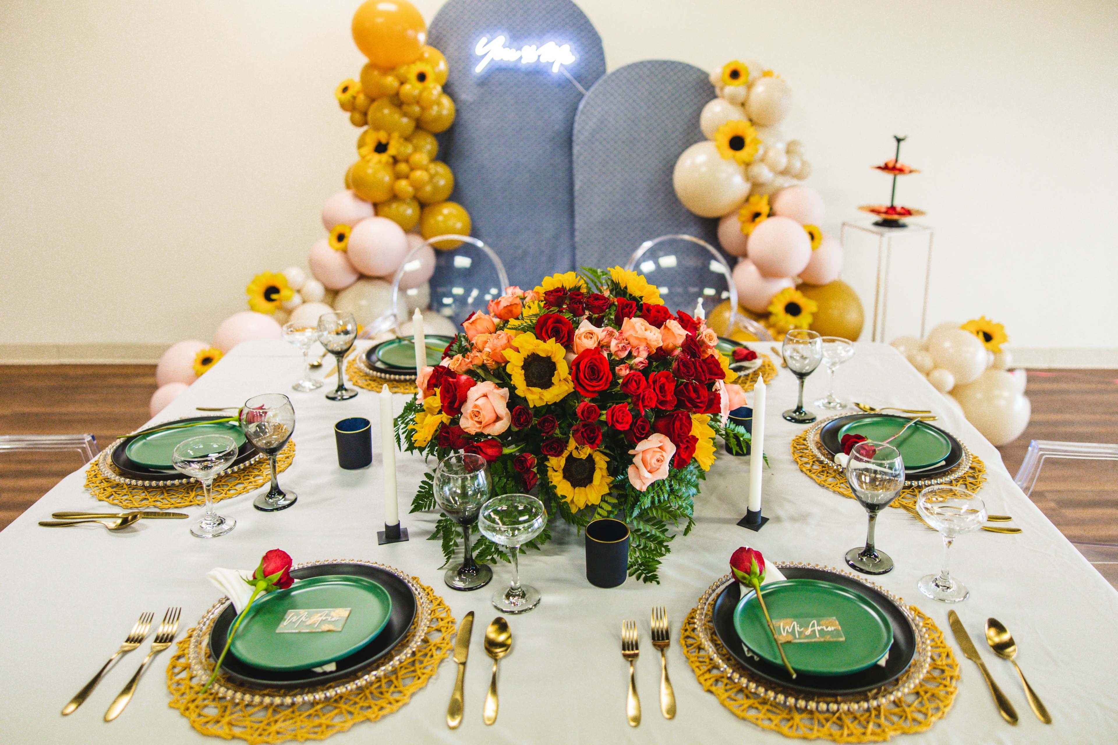 A decorated dining table features green plates, floral centerpieces, and a backdrop of balloons and neon lights.