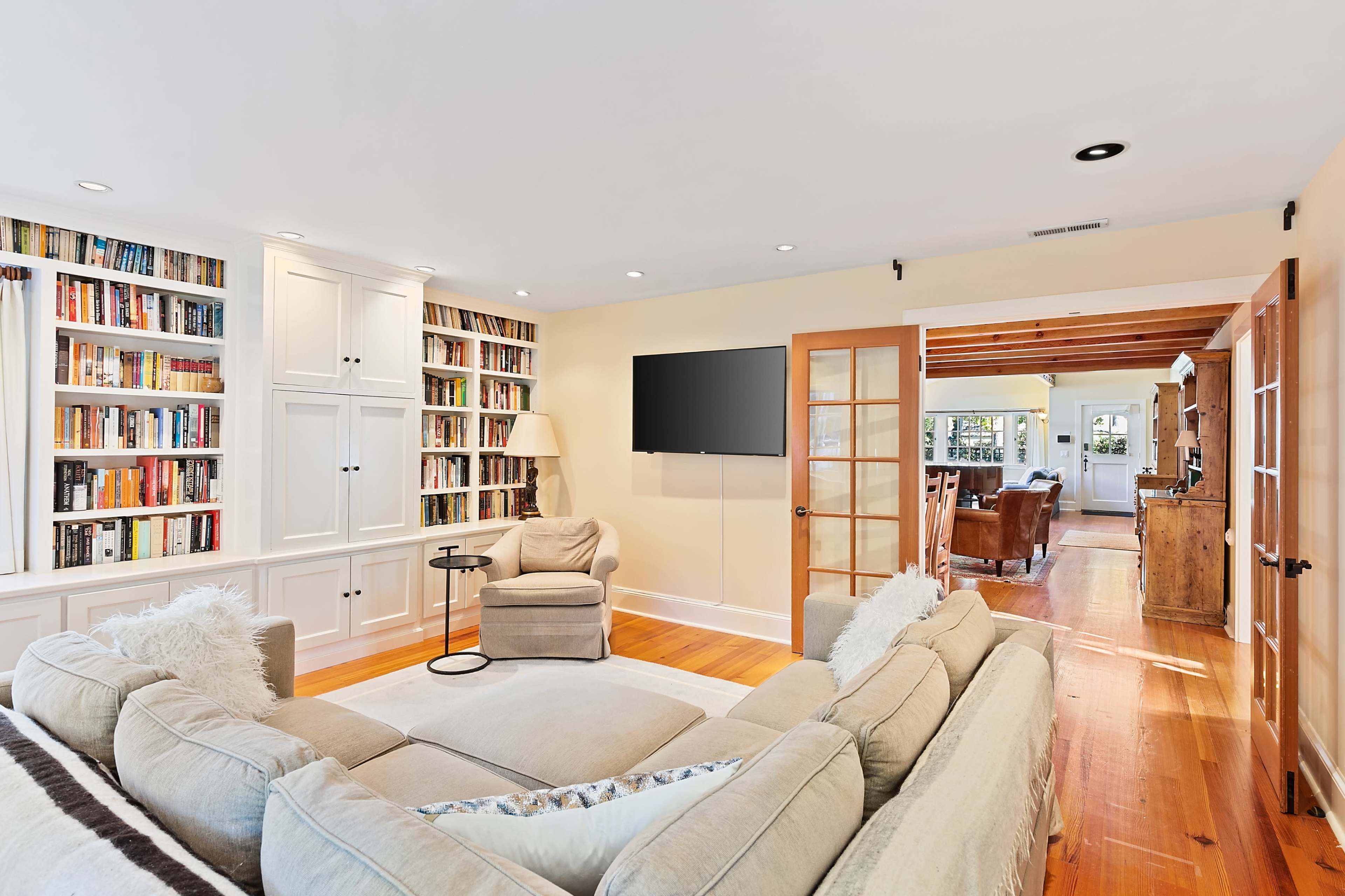 The living room features a large sectional sofa facing a mounted television, with a built-in bookshelf filled with books, and an open doorway leading to another room.