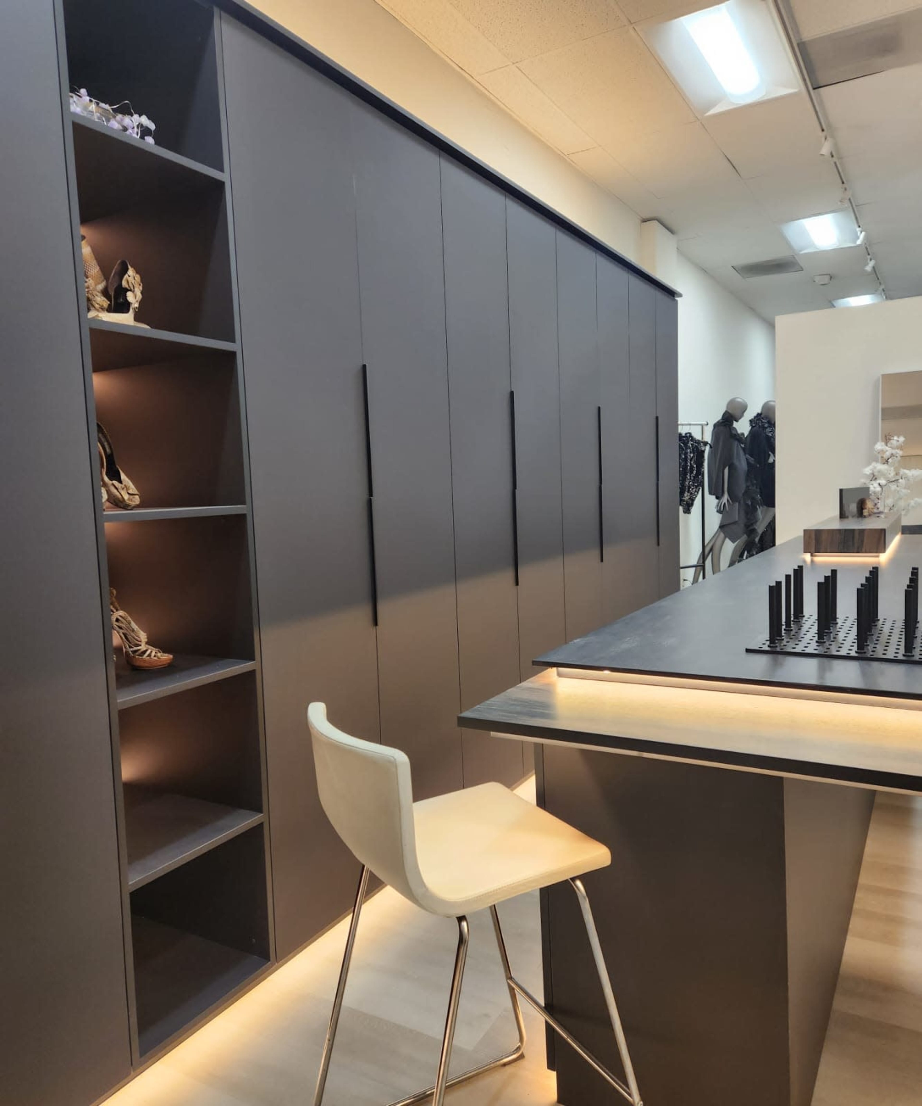 The image shows a modern retail space with sleek cabinetry, displaying shoes on the left, and a minimalist counter with a chair on the right.