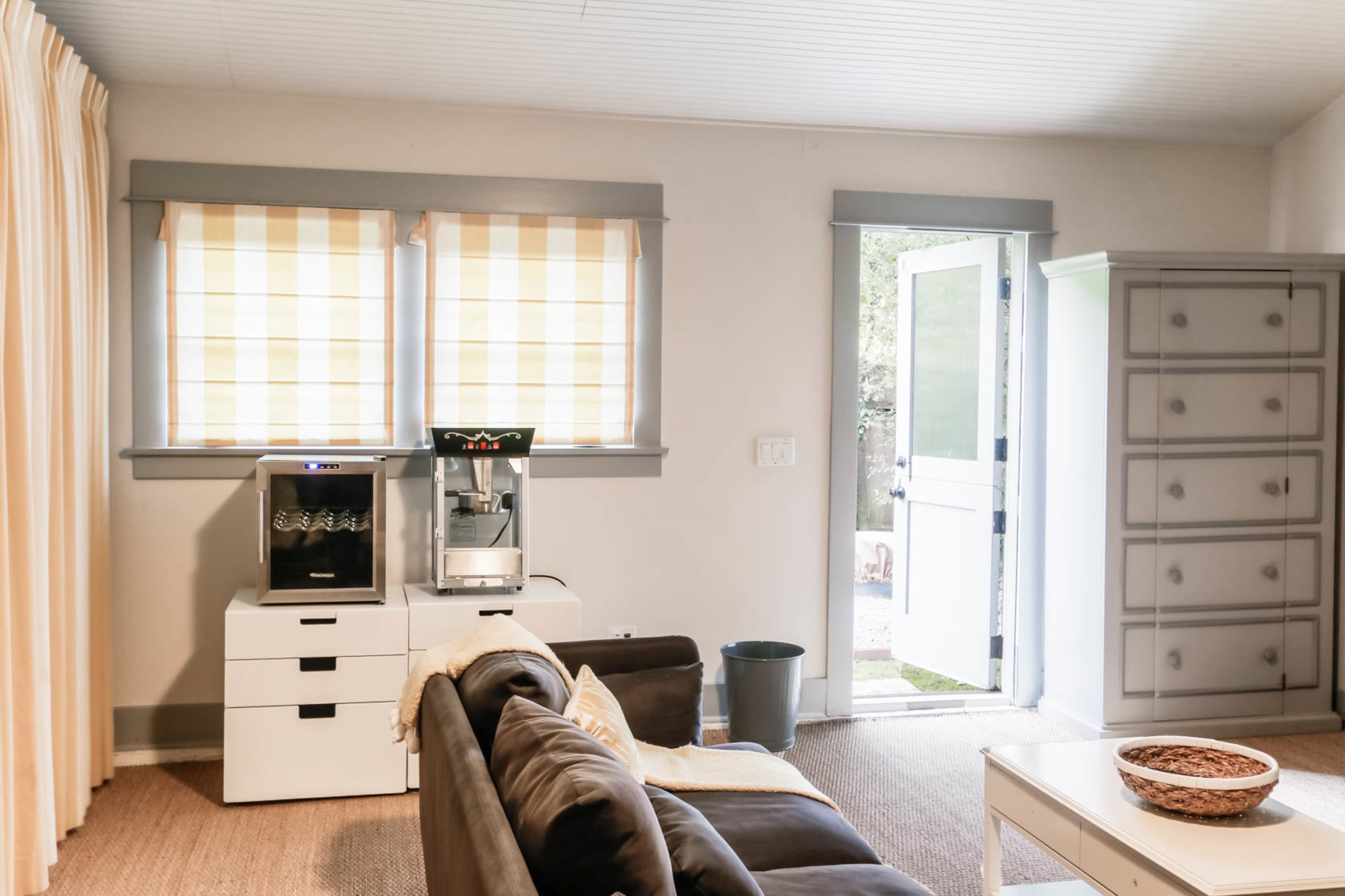 A living room with a dark sofa, a beverage station, and a doorway leading outside.