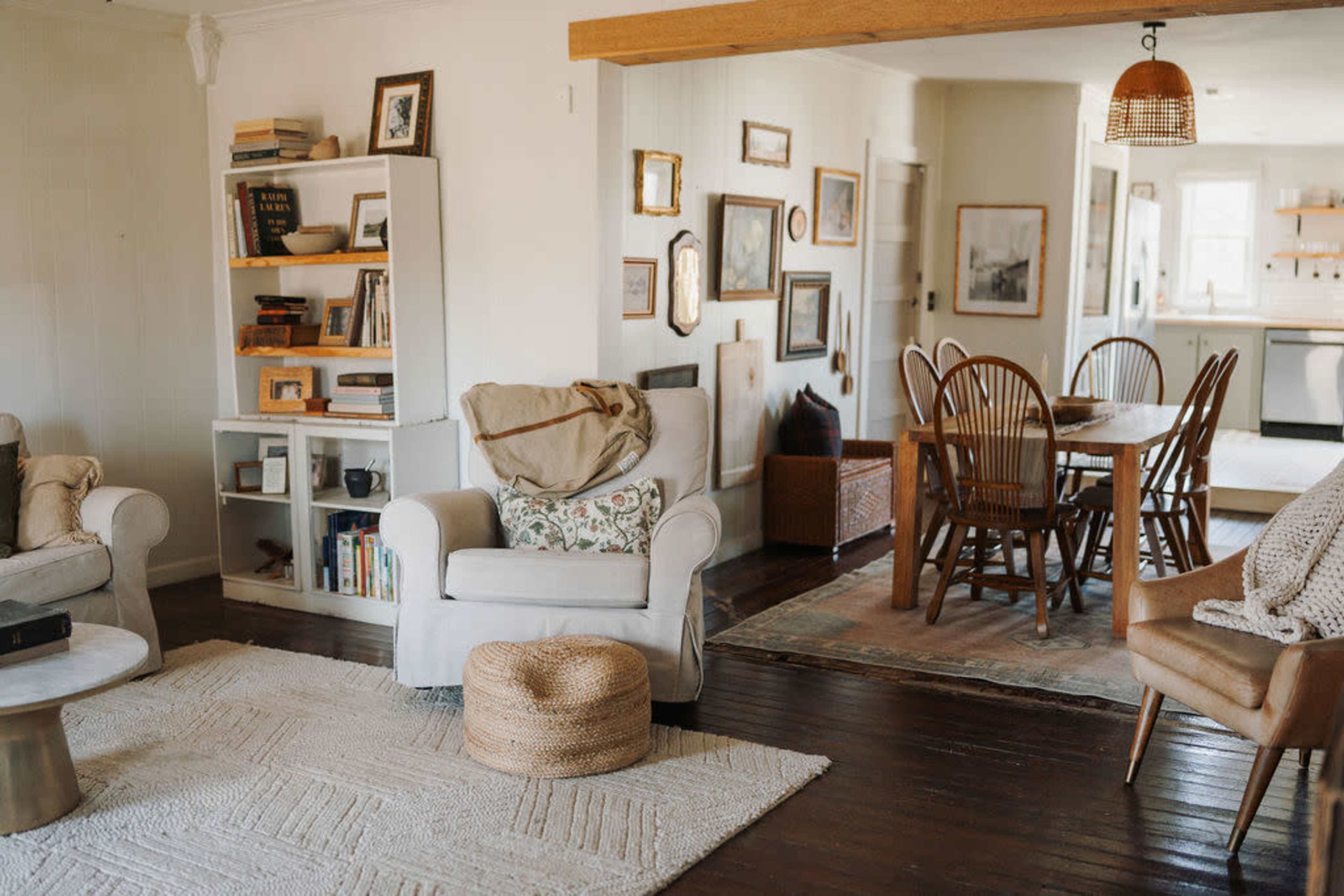 The image shows a cozy living area featuring comfortable seating, a bookshelf filled with books, and a dining table surrounded by wooden chairs.