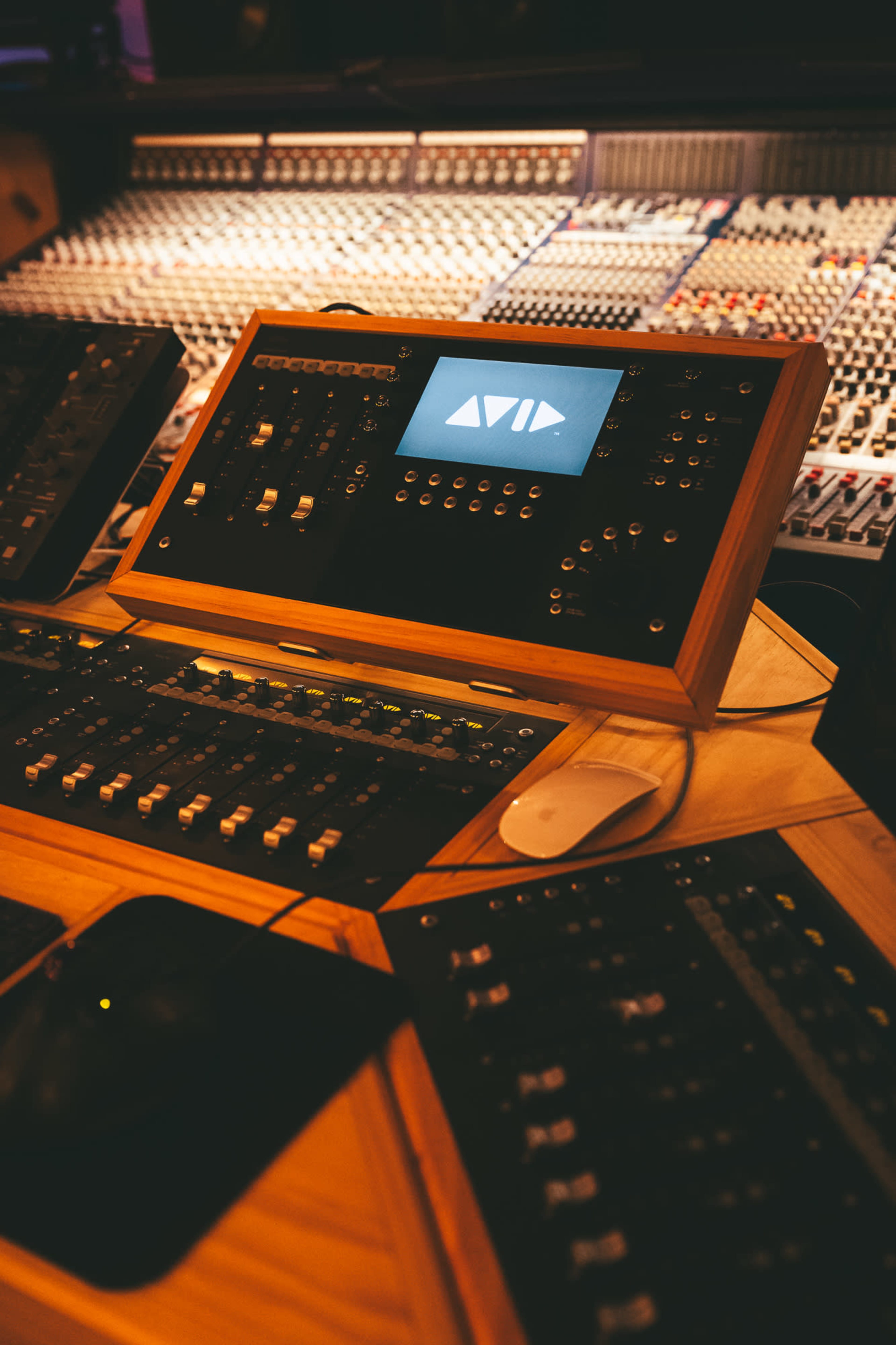 The image shows a control panel with various knobs and buttons, situated in a sound recording studio alongside a large mixer.