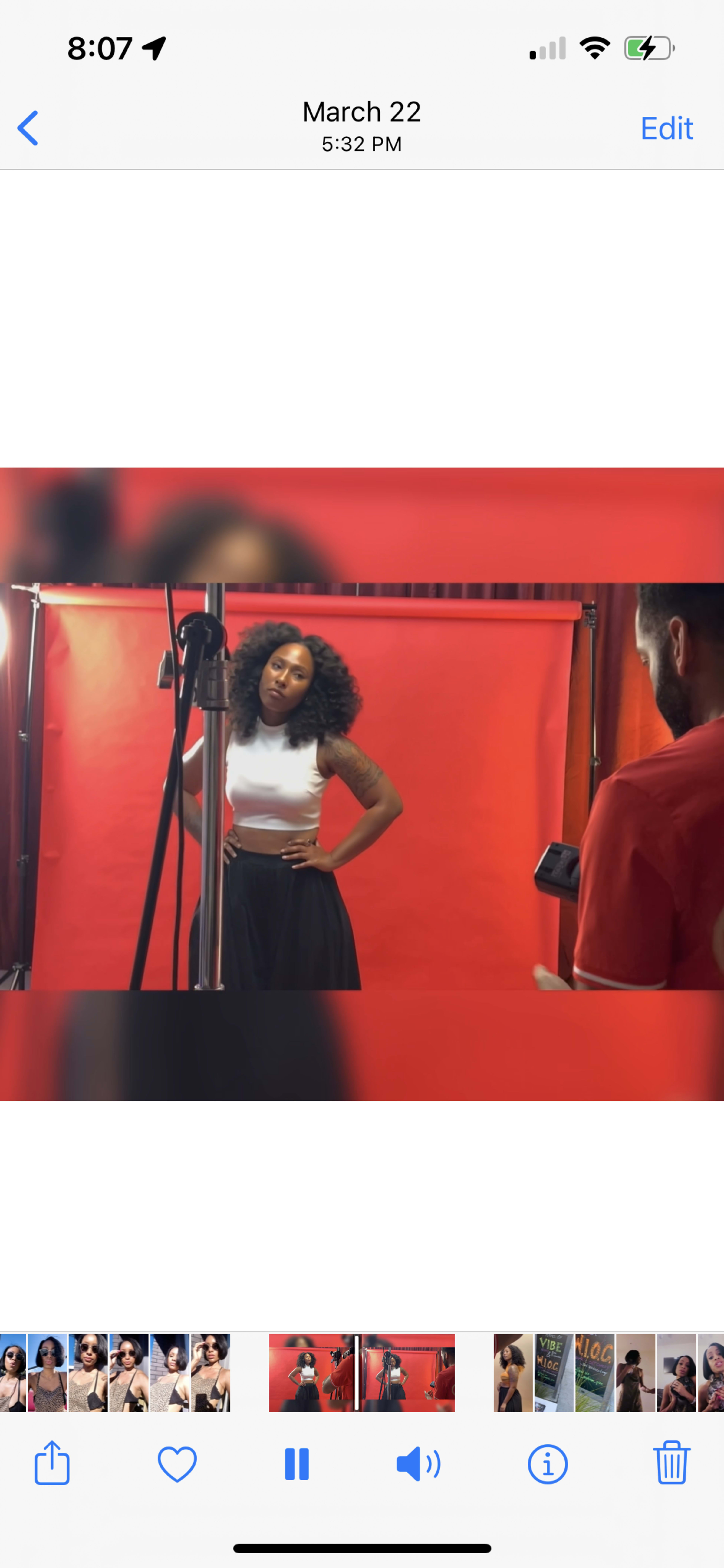 A woman poses in front of a red backdrop while a photographer adjusts equipment nearby.