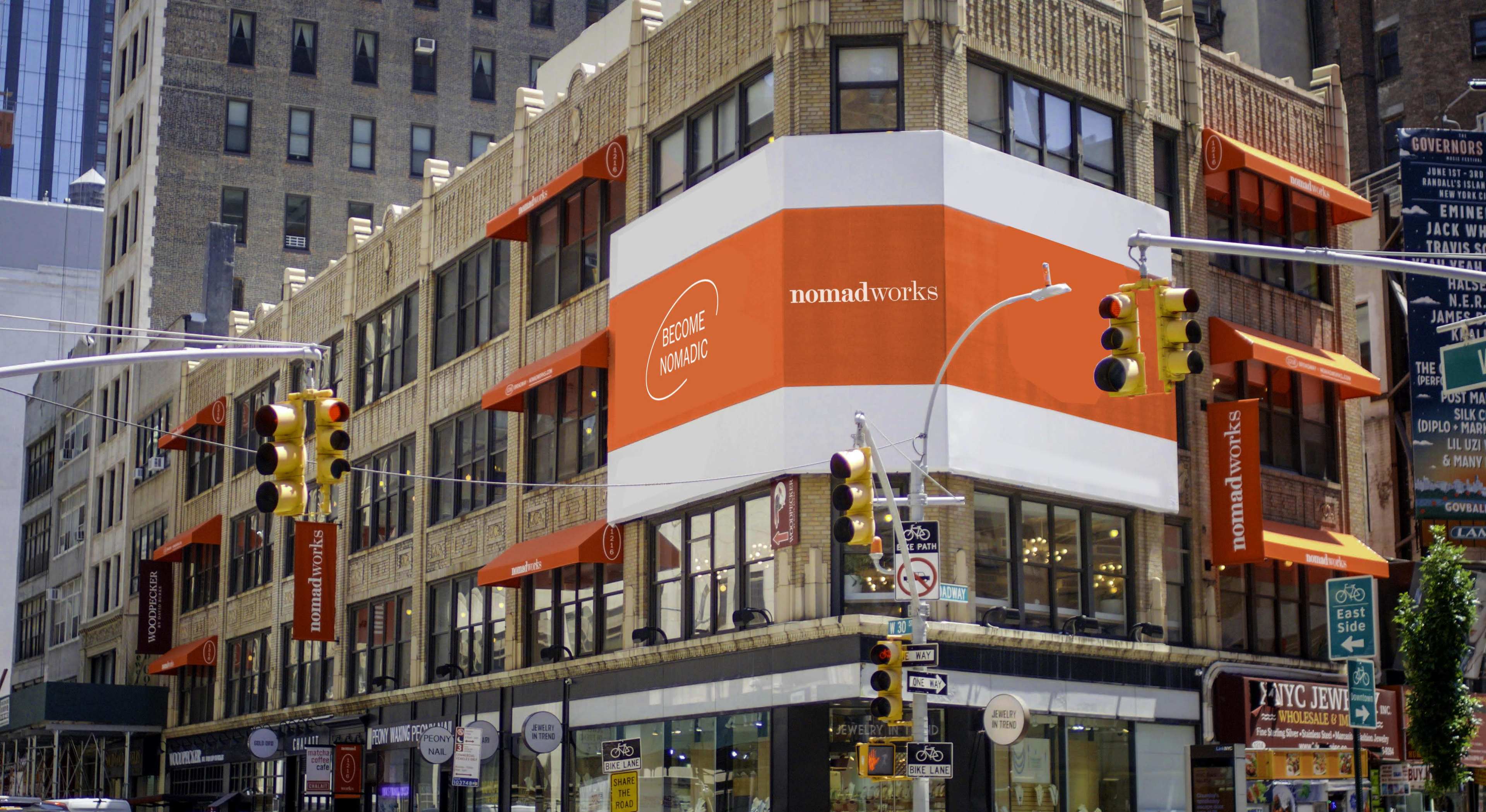 A multi-story building with a large orange and white sign displaying "nomadworks" on the corner, along with several traffic lights and banners hanging from the facade.