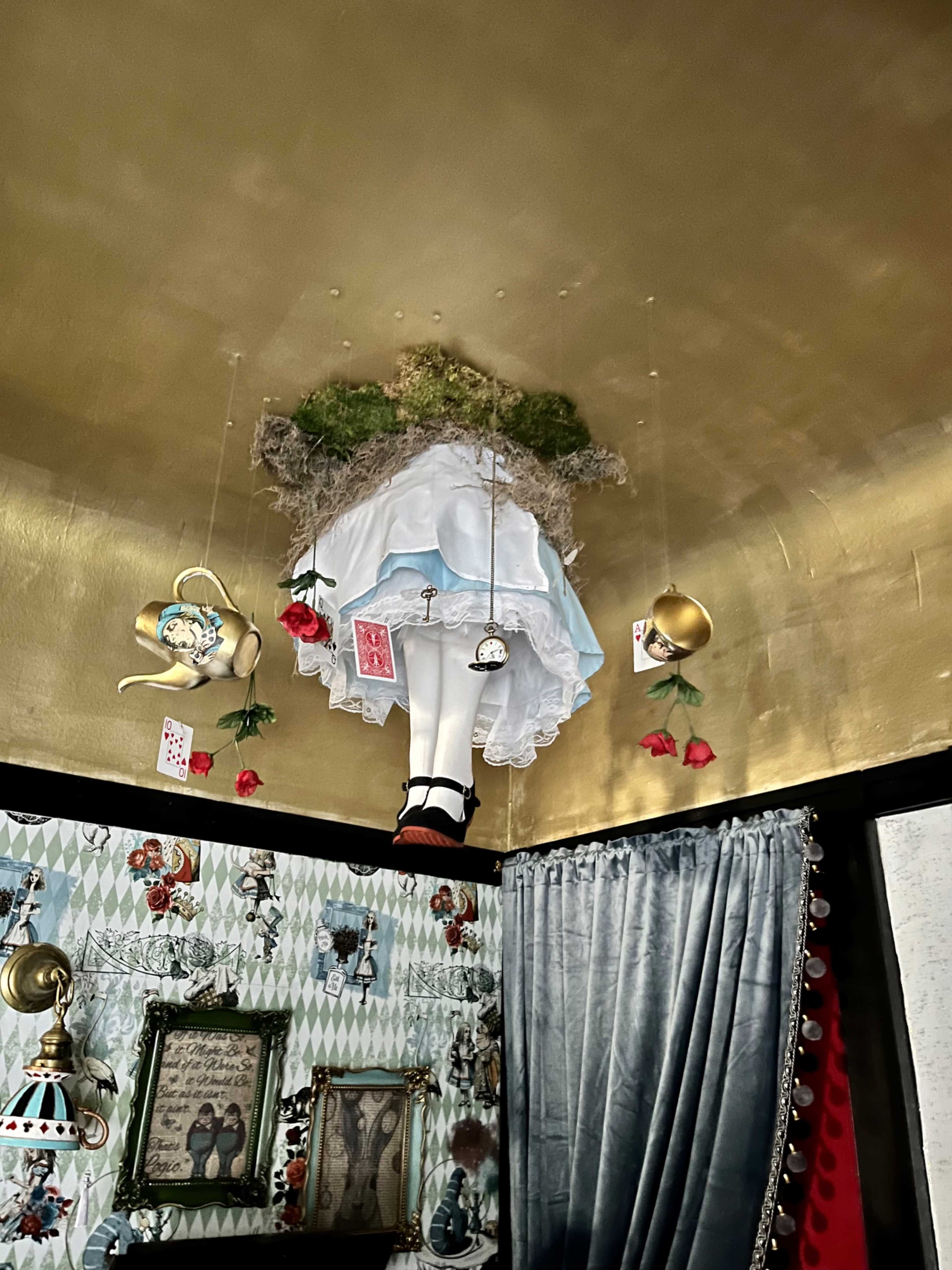 The ceiling features a mannequin dressed in a white dress and red shoes, surrounded by hanging decorations and floral elements.