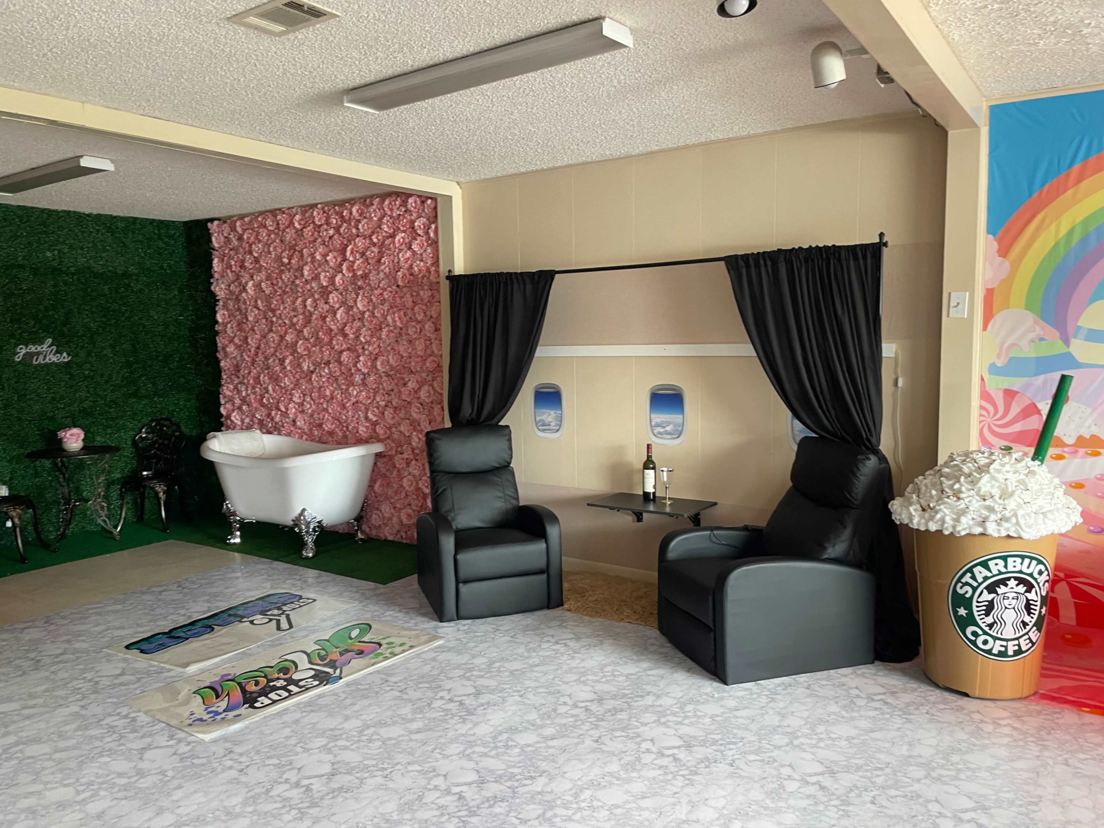 The image shows a room set up with two black reclining chairs, a bathtub, and a colorful wall featuring a Starbucks cup design and a pink floral backdrop.