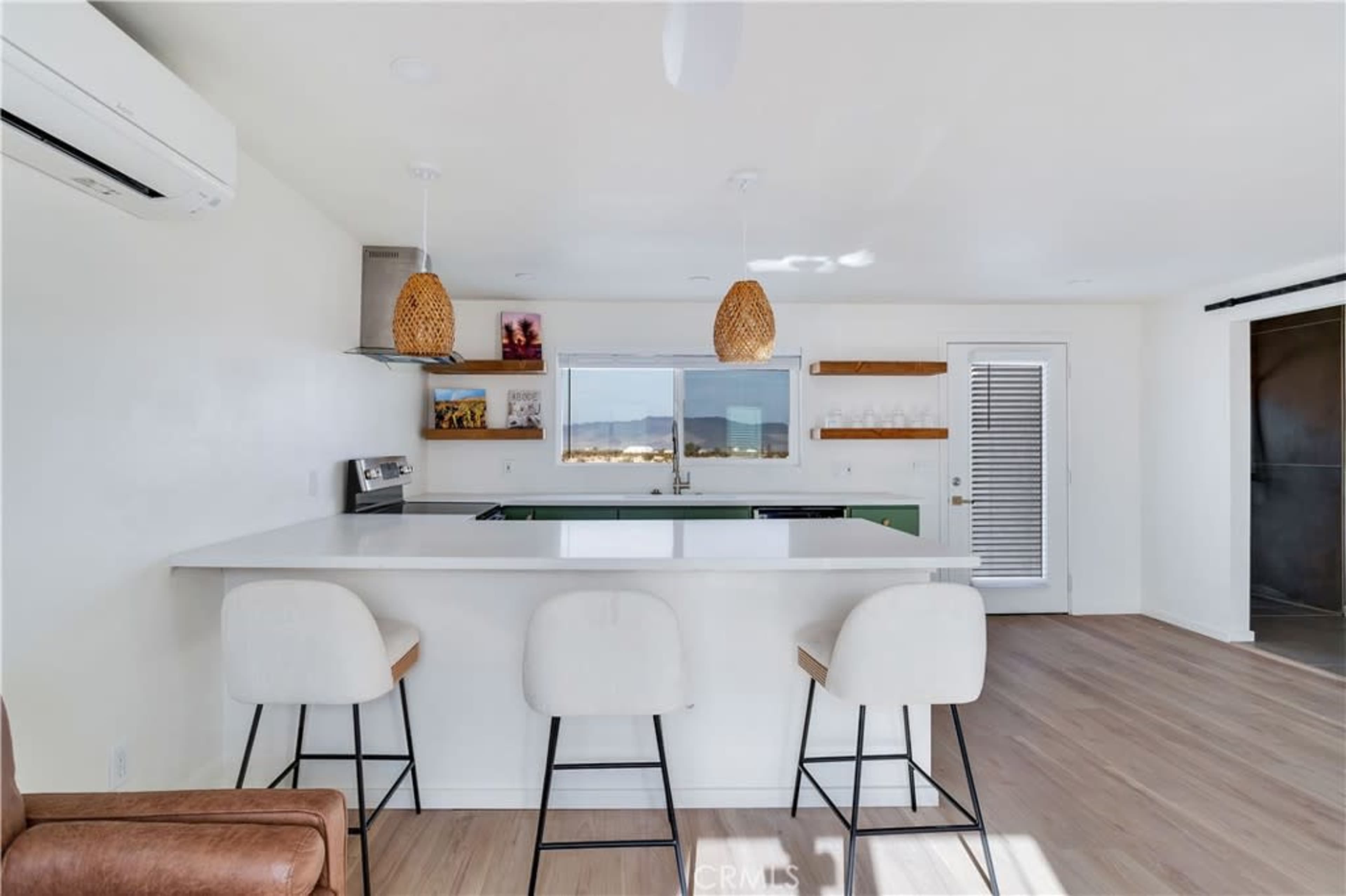 A modern kitchen features a white bar with three stools, open shelving, and a large window with mountain views.