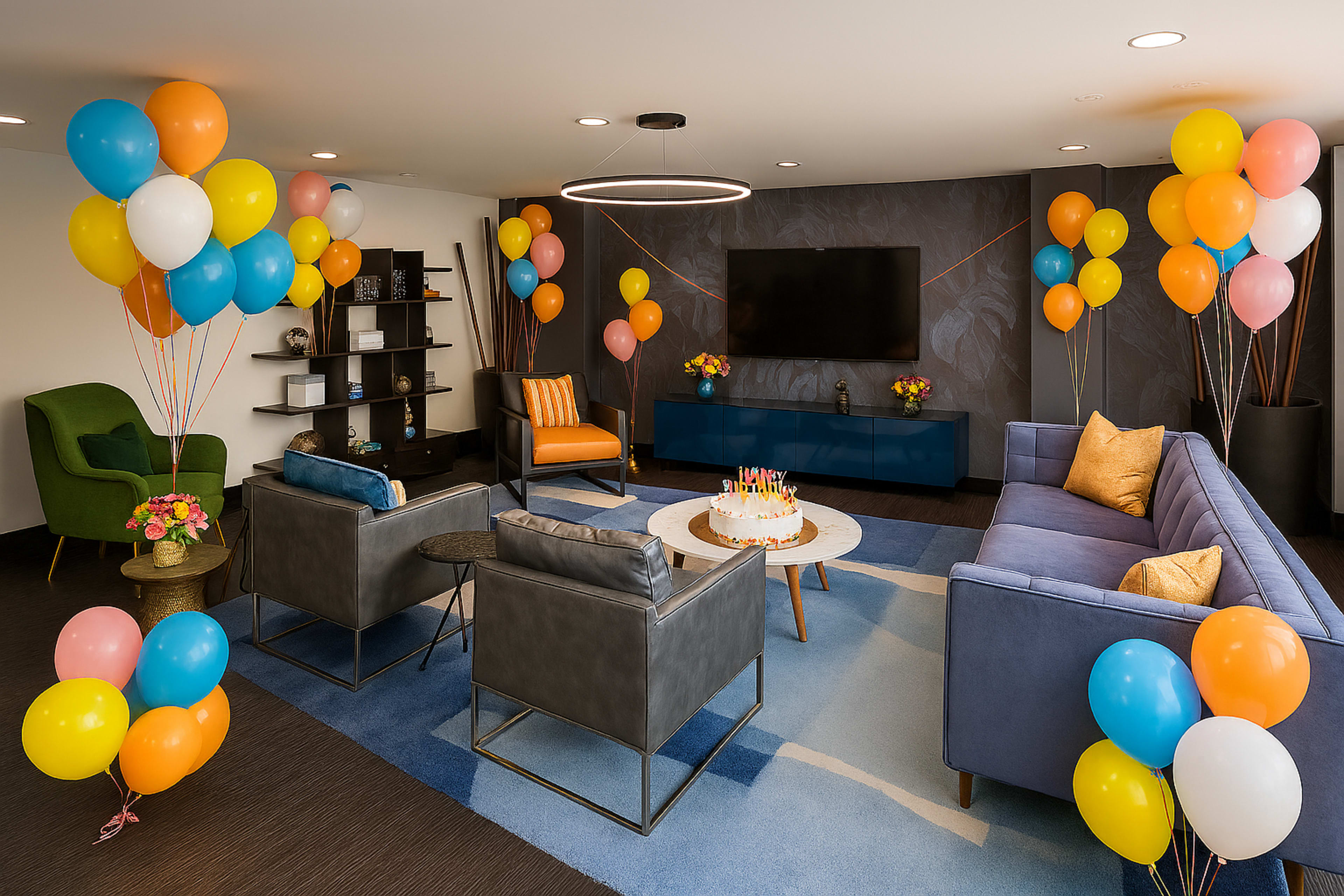 The image depicts a colorful party scene with a birthday cake on a circular table surrounded by modern seating, decorated with balloons in various colors.