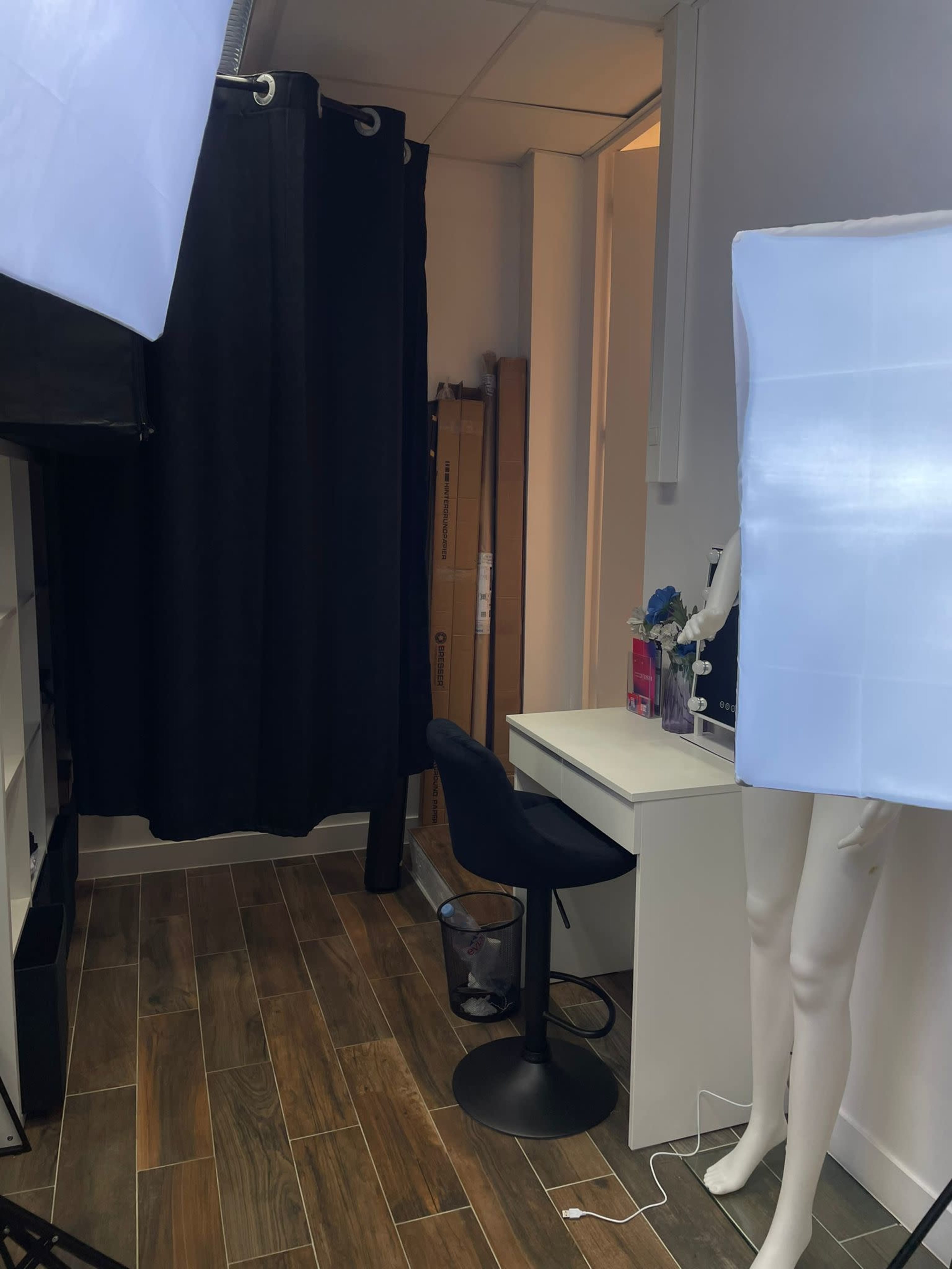 The scene shows a small room with a black curtain, a desk with a chair, and lighting equipment on either side.