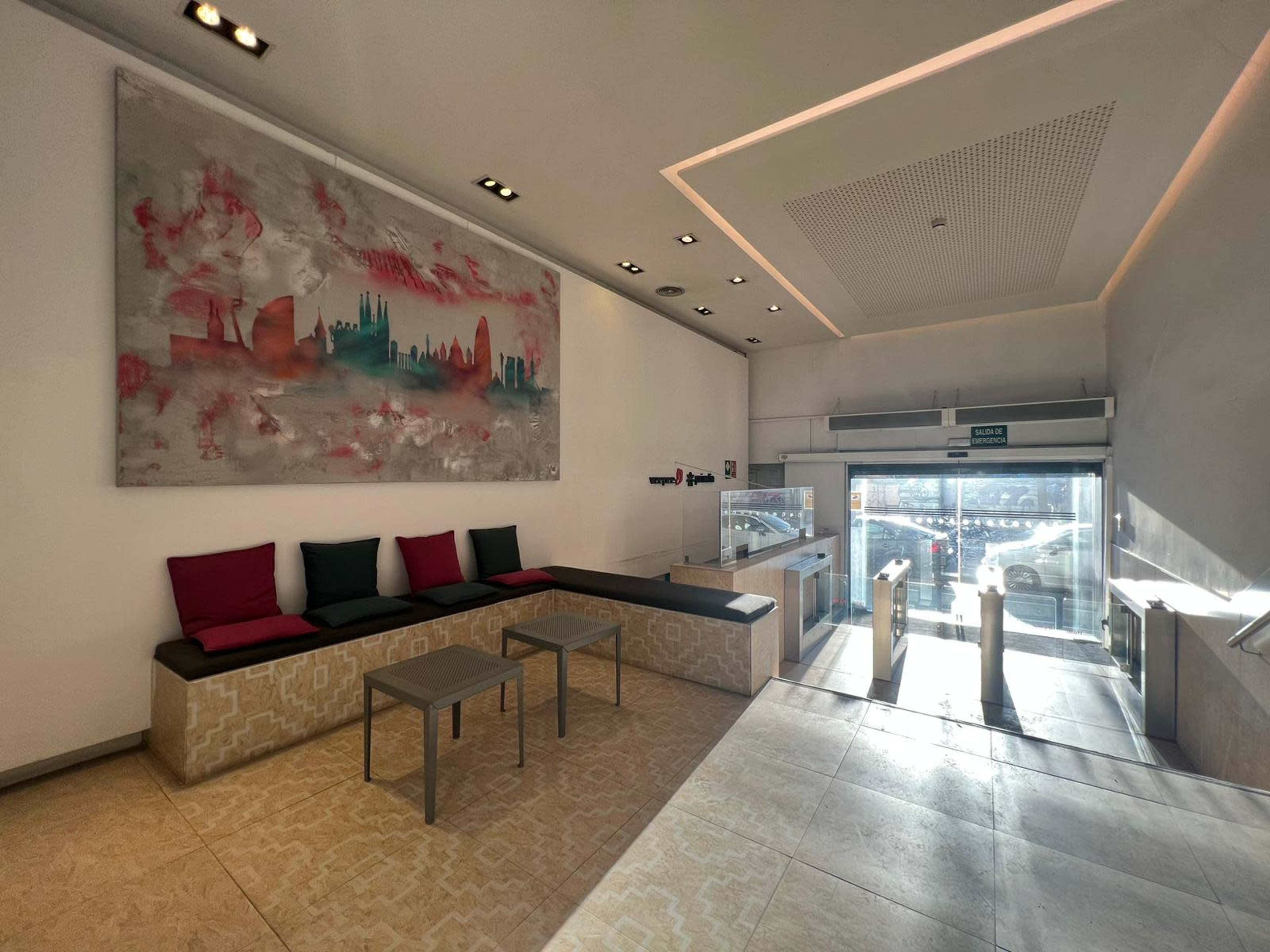 A modern indoor lobby area with a large abstract painting on the wall, seating along one side, and glass doors leading outside.
