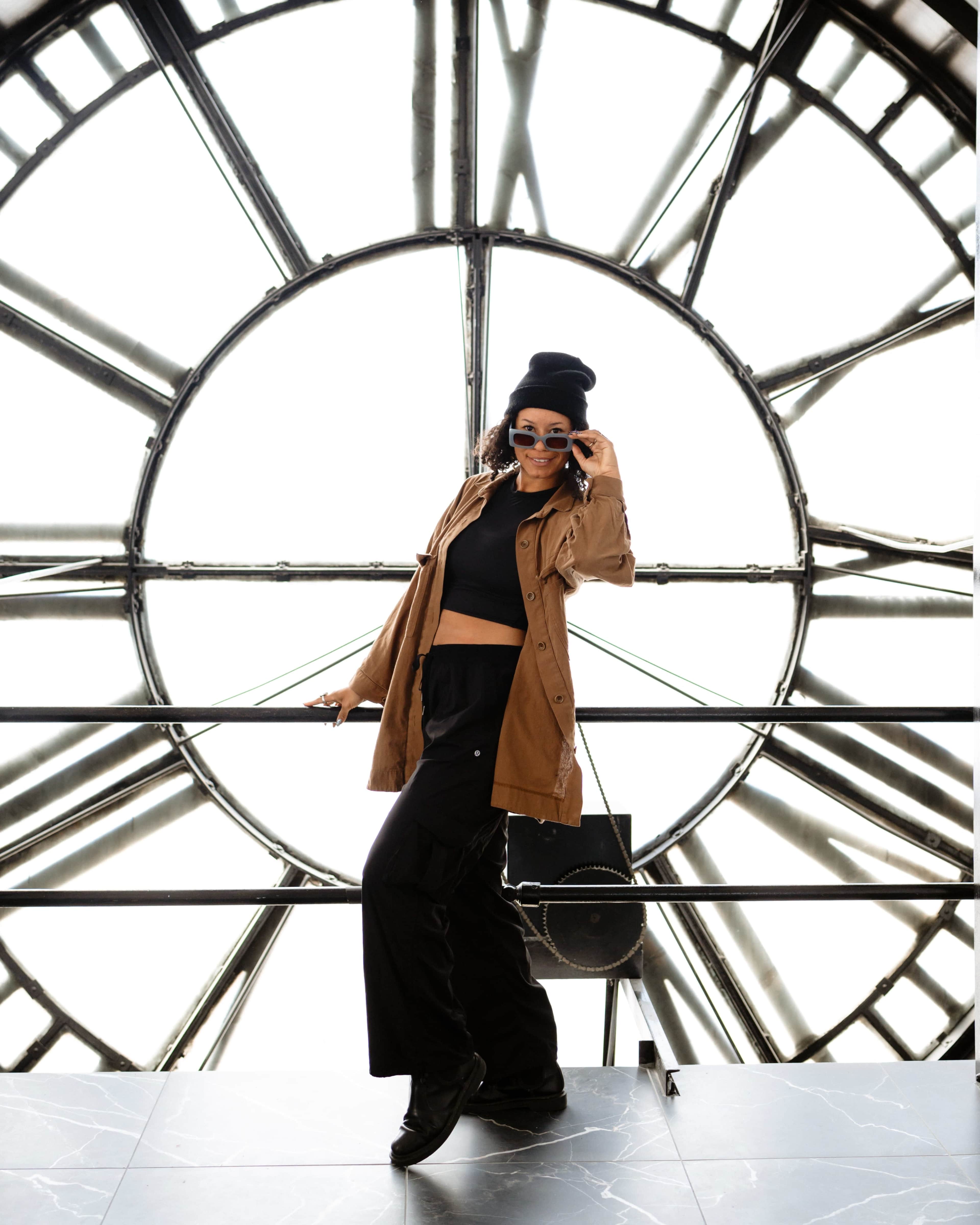 A person poses confidently against the backdrop of a large clock face.