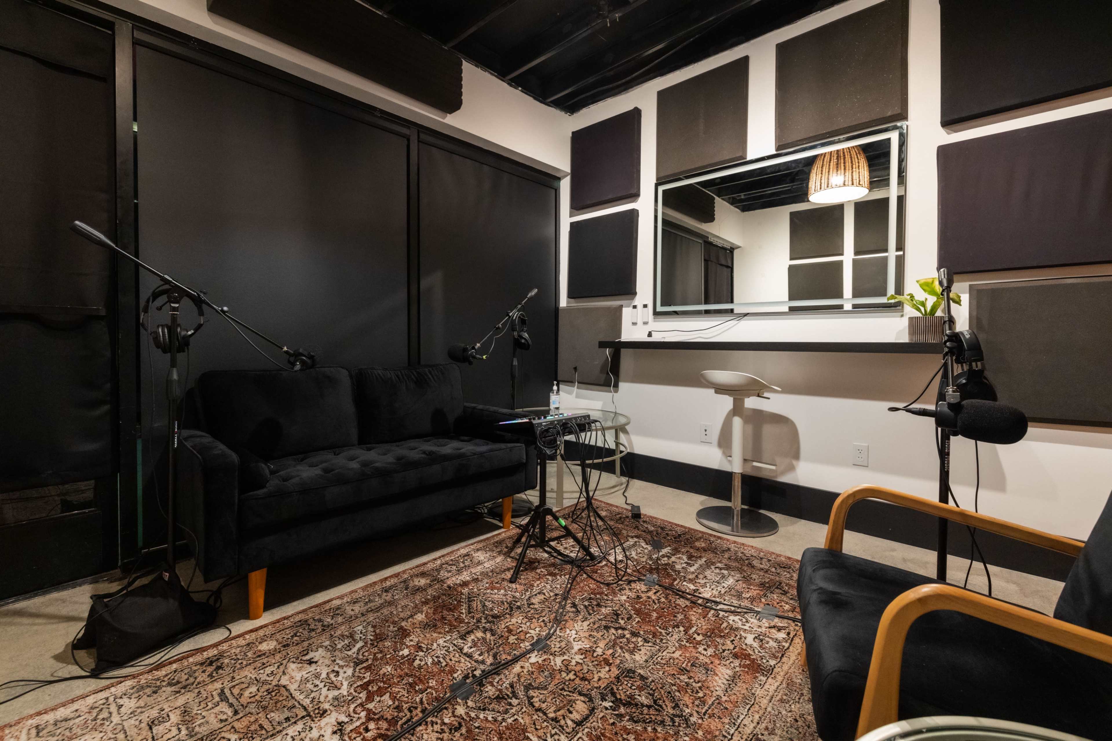 A recording studio with a dark couch, microphones set up, and a rug on the floor.