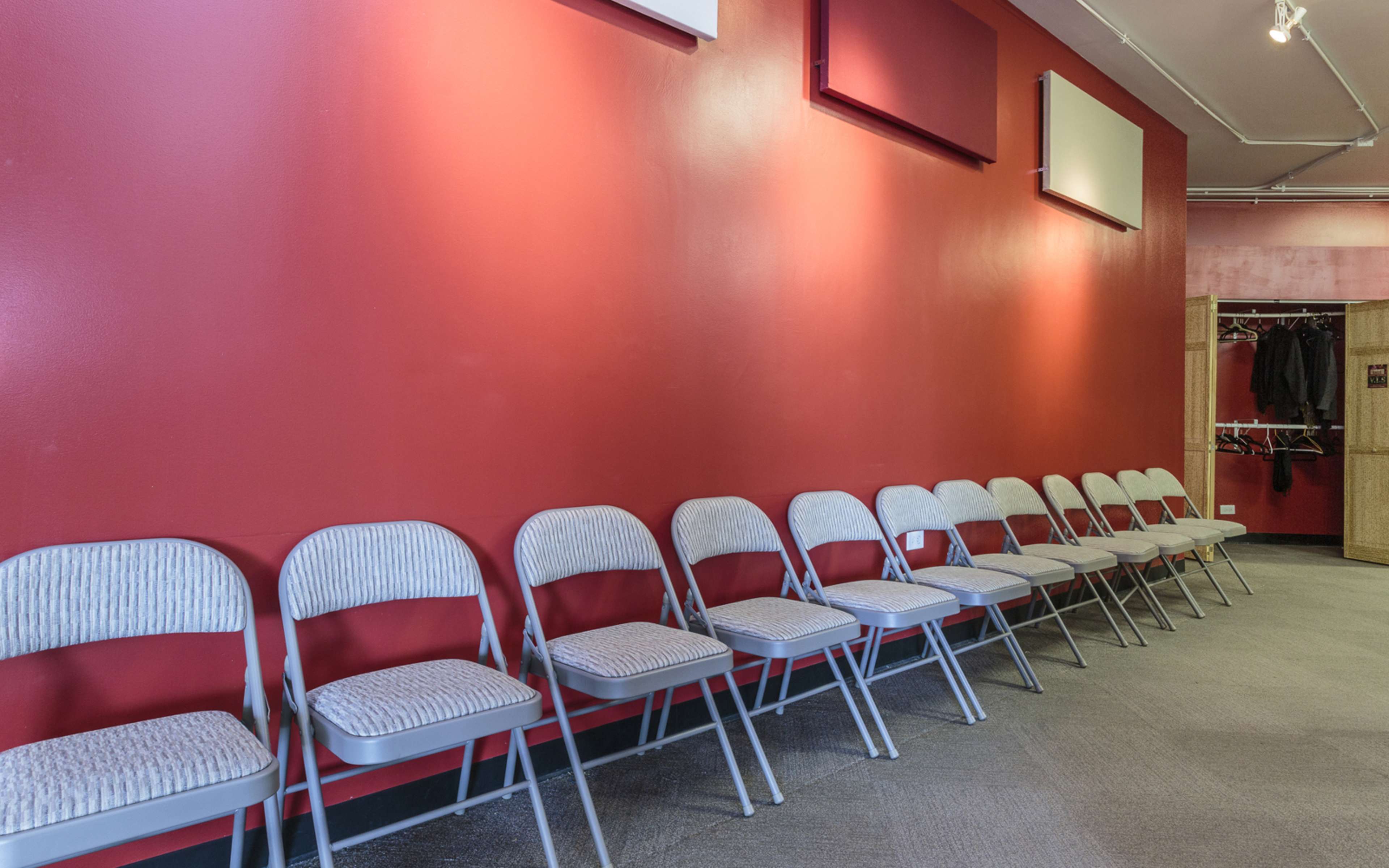A row of eight folding chairs is positioned along a red wall in a largely empty room.