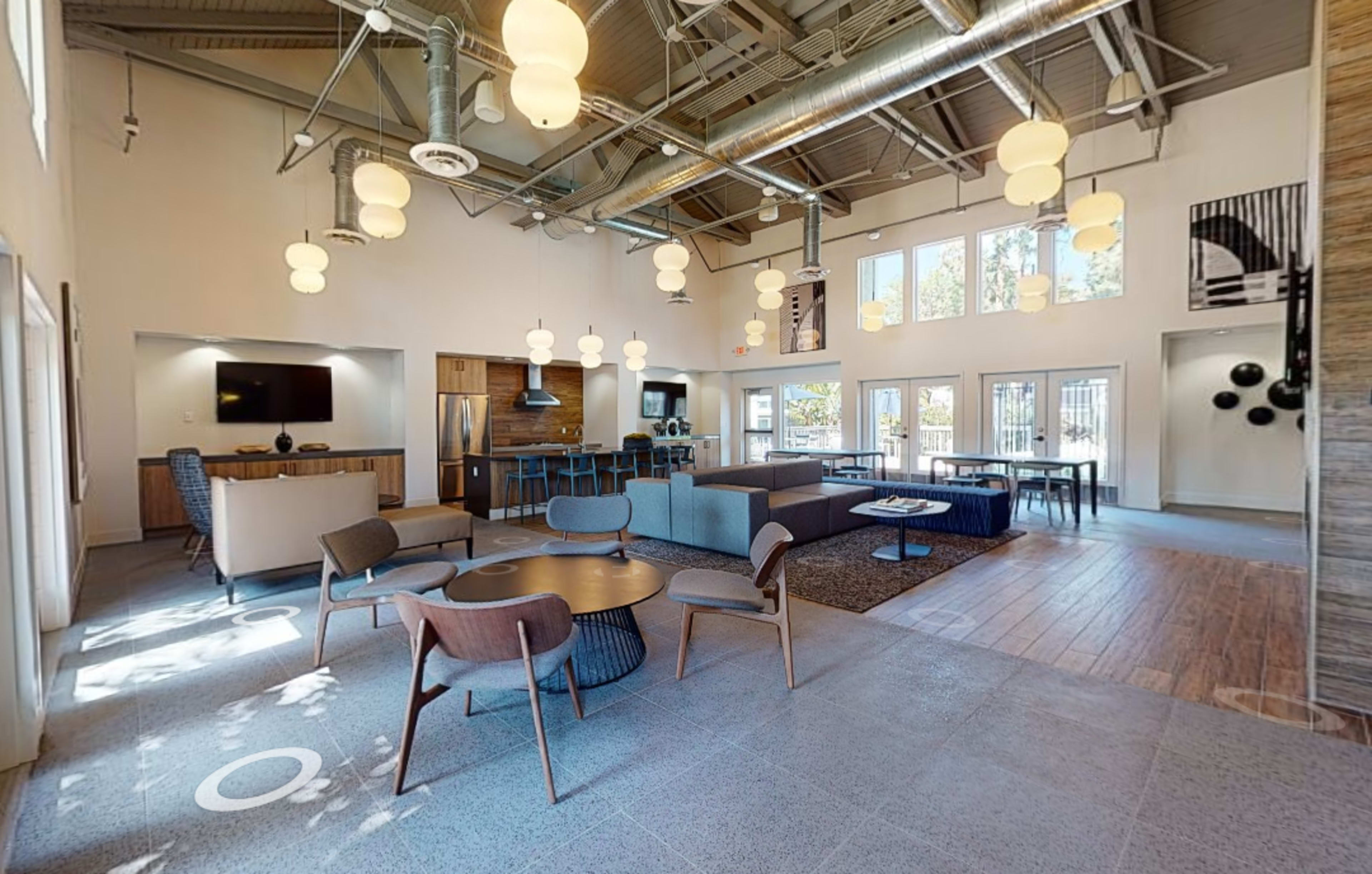 An interior space with a lounge area featuring seating, tables, and large windows that allow natural light to enter.