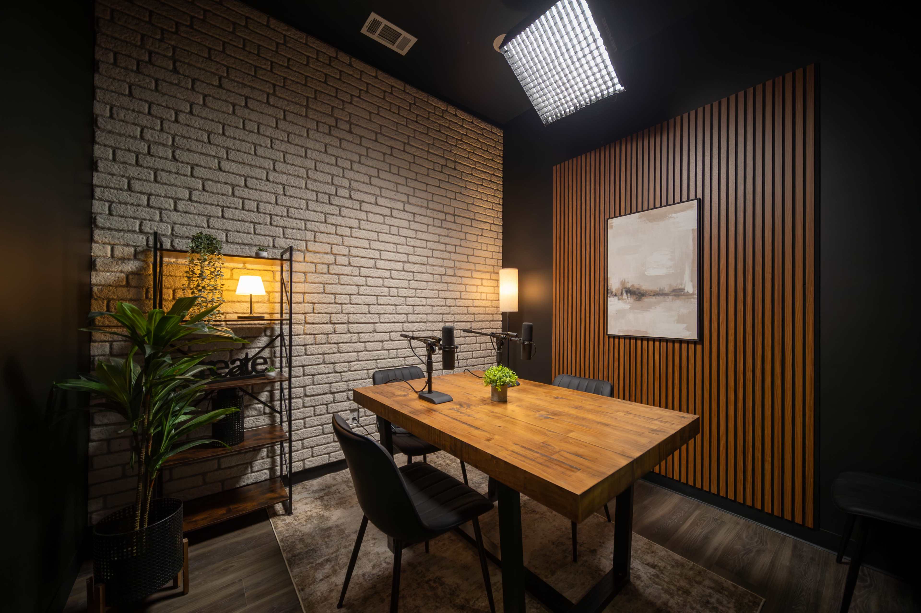A modern conference room features a wooden table surrounded by black chairs, a potted plant, and decorative lighting against a backdrop of textured walls.