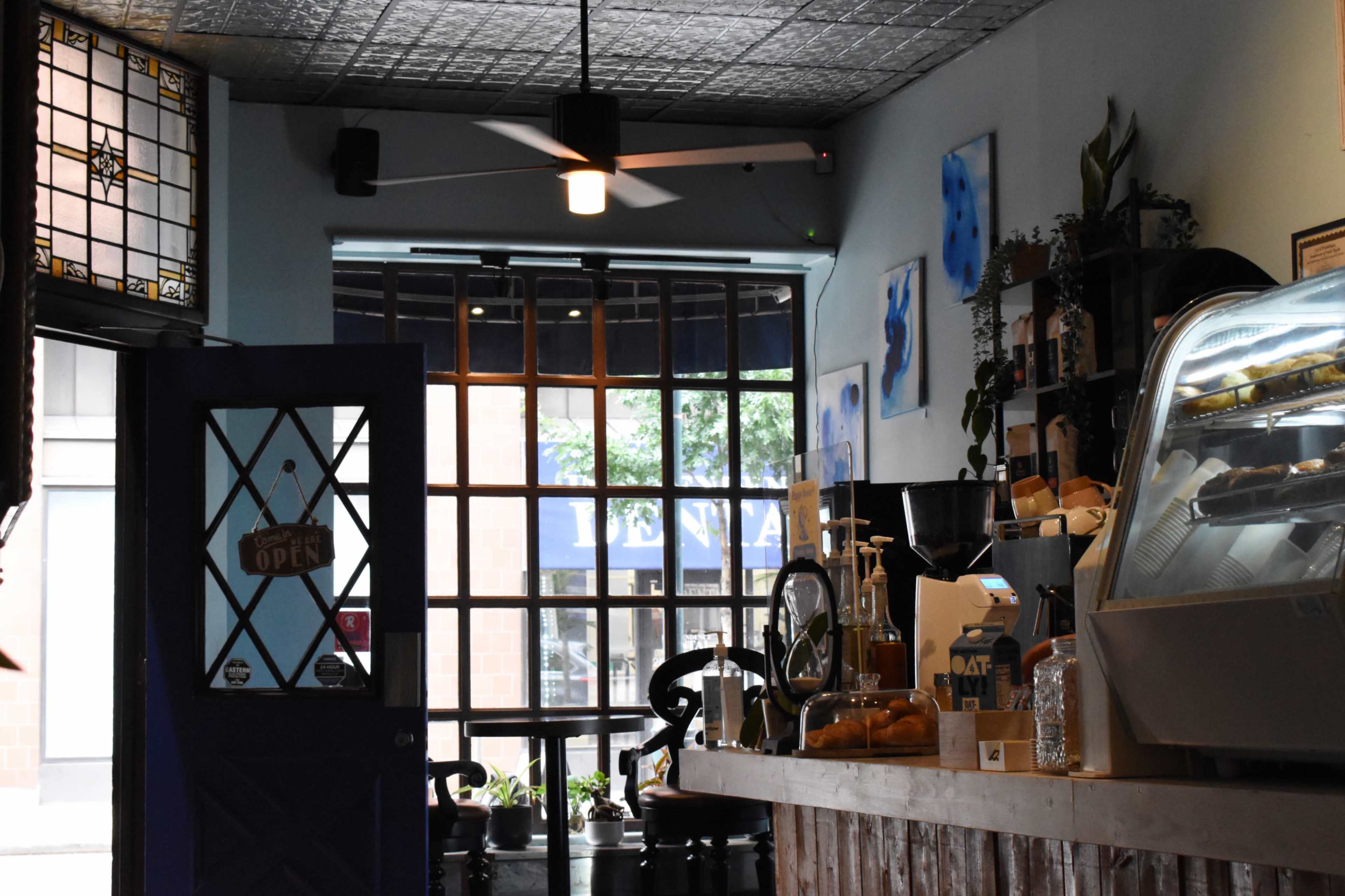 A coffee shop interior with a glass door labeled "OPEN," a counter displaying pastries, and large windows that let in natural light.