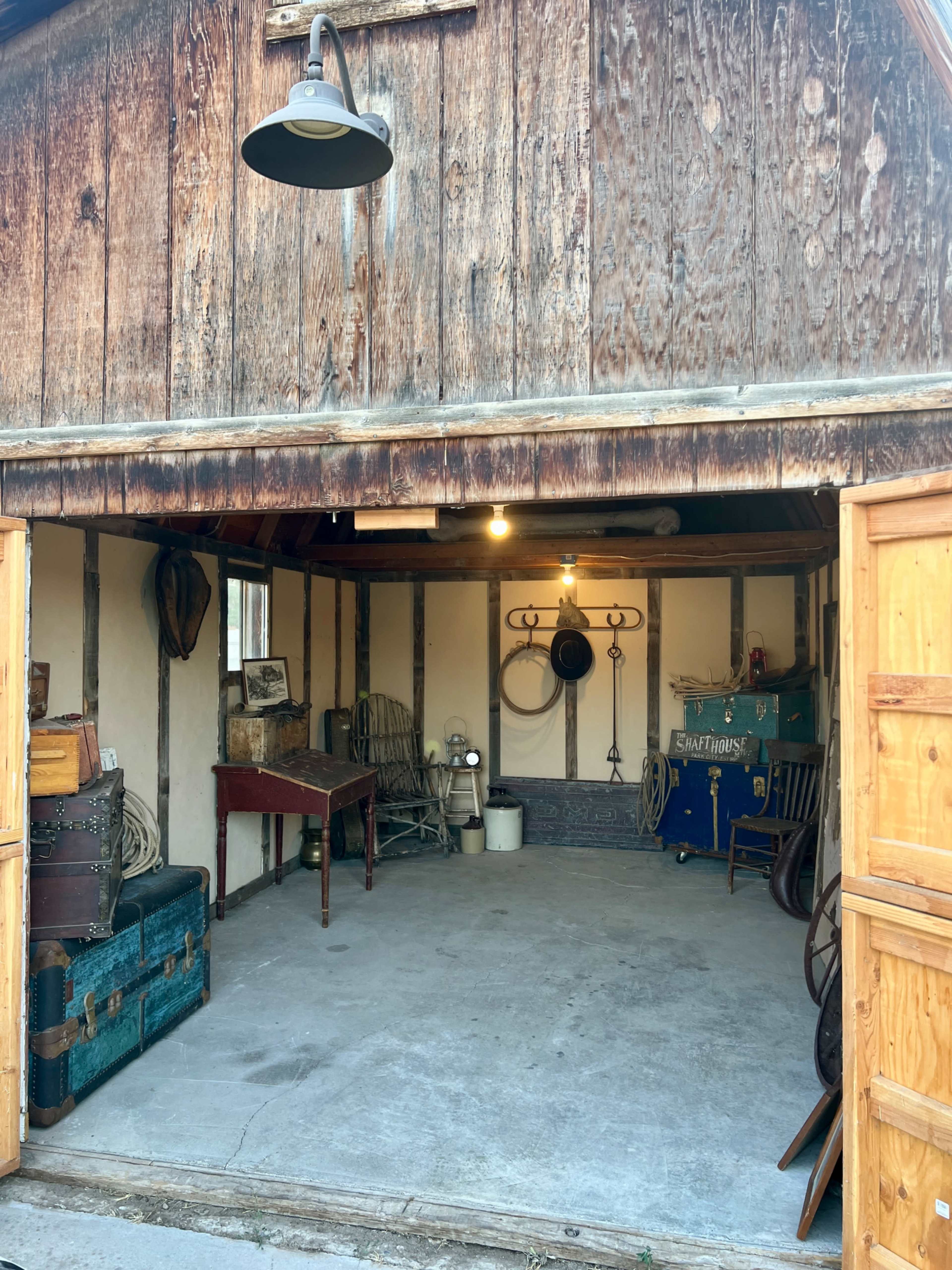 The image shows a partially open garage with a wooden exterior, revealing a cluttered interior containing various vintage items and furniture.