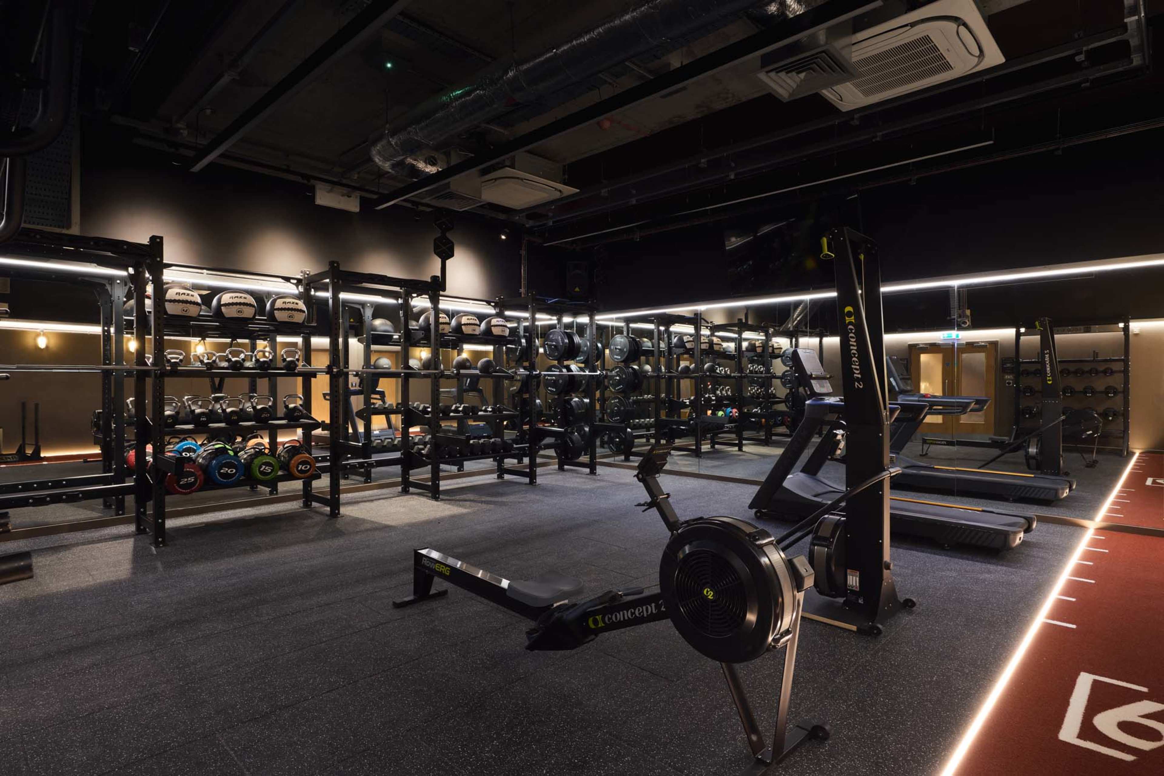 The image shows a modern gym interior with weight racks, cardio machines, and a designated workout area.