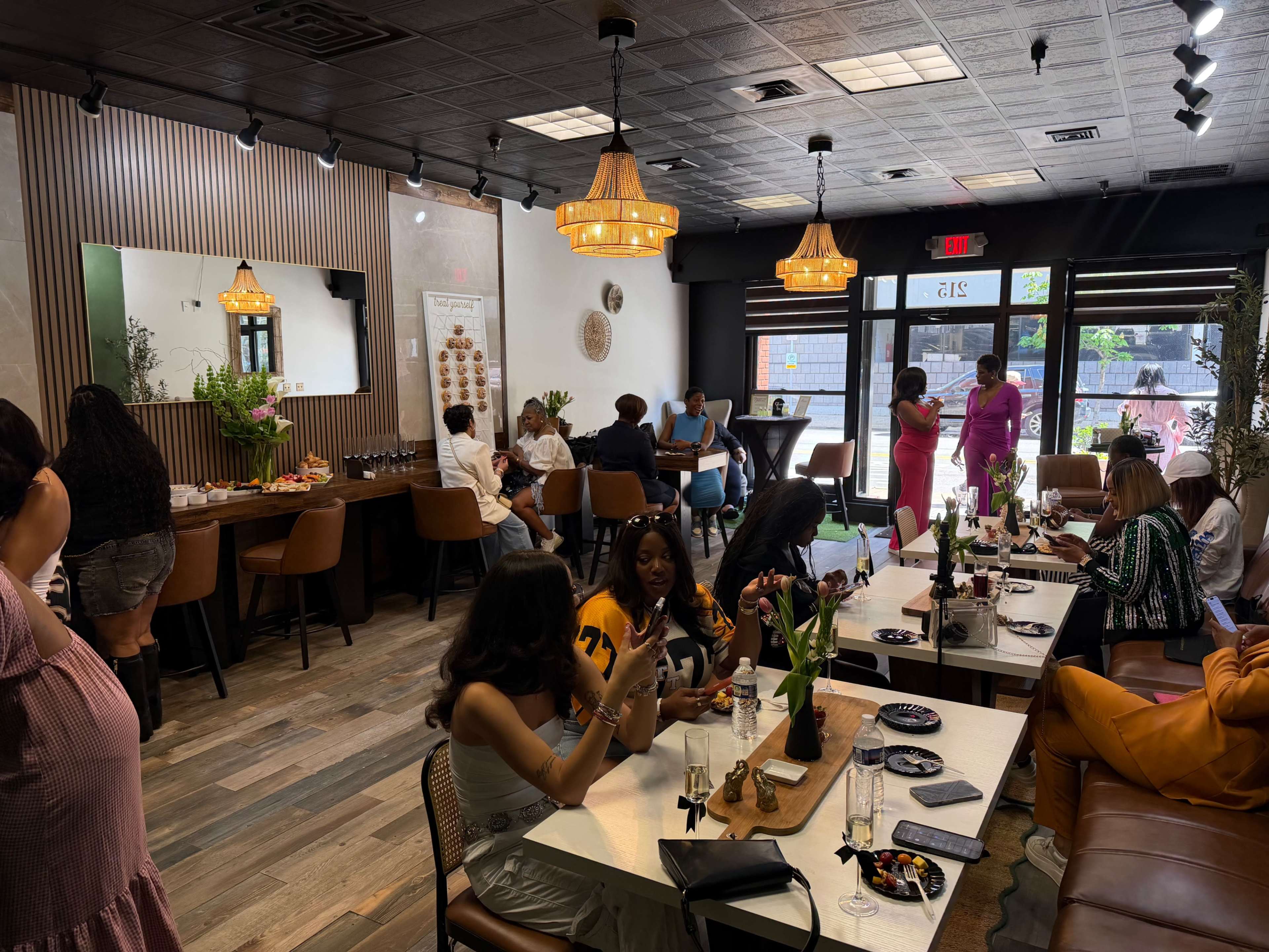 The image shows a busy café interior with patrons seated at tables, some engaging in conversation, while others enjoy food and drinks.