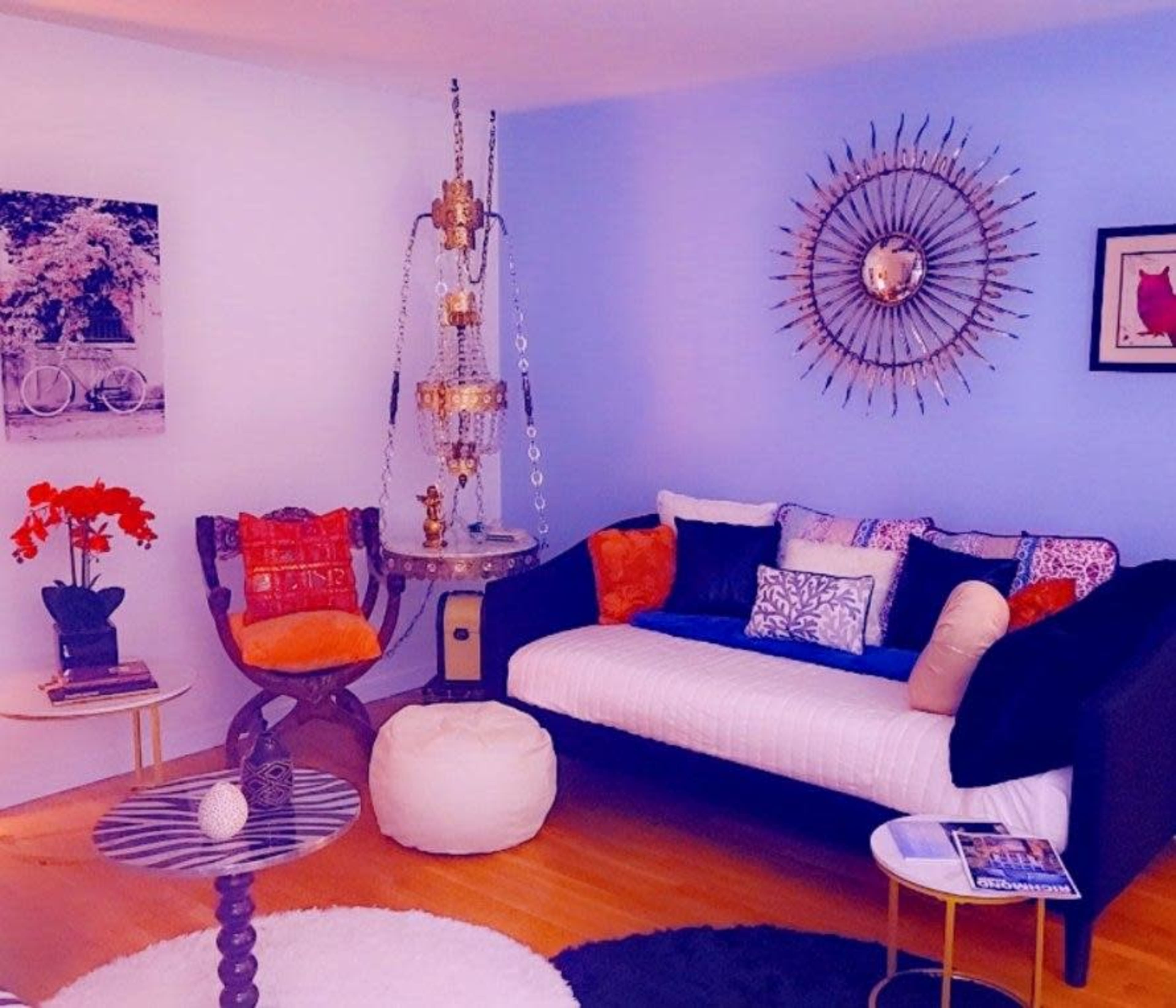 The living room features a black sofa with decorative pillows, a round coffee table, a pouf, and a standing lamp with an ornate design.