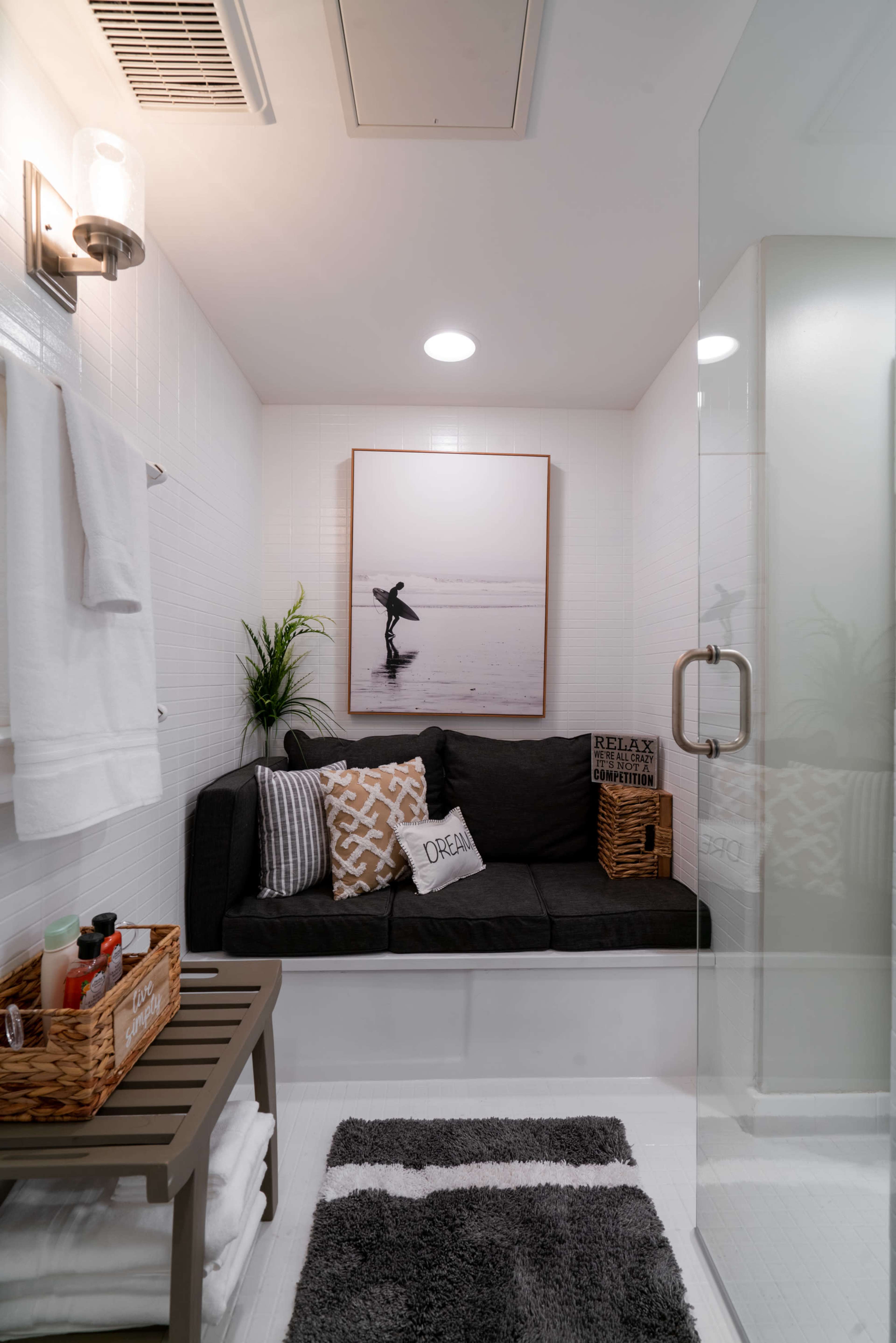 A modern bathroom featuring a glass shower, a cozy sitting area with cushions, and a framed photograph on the wall.