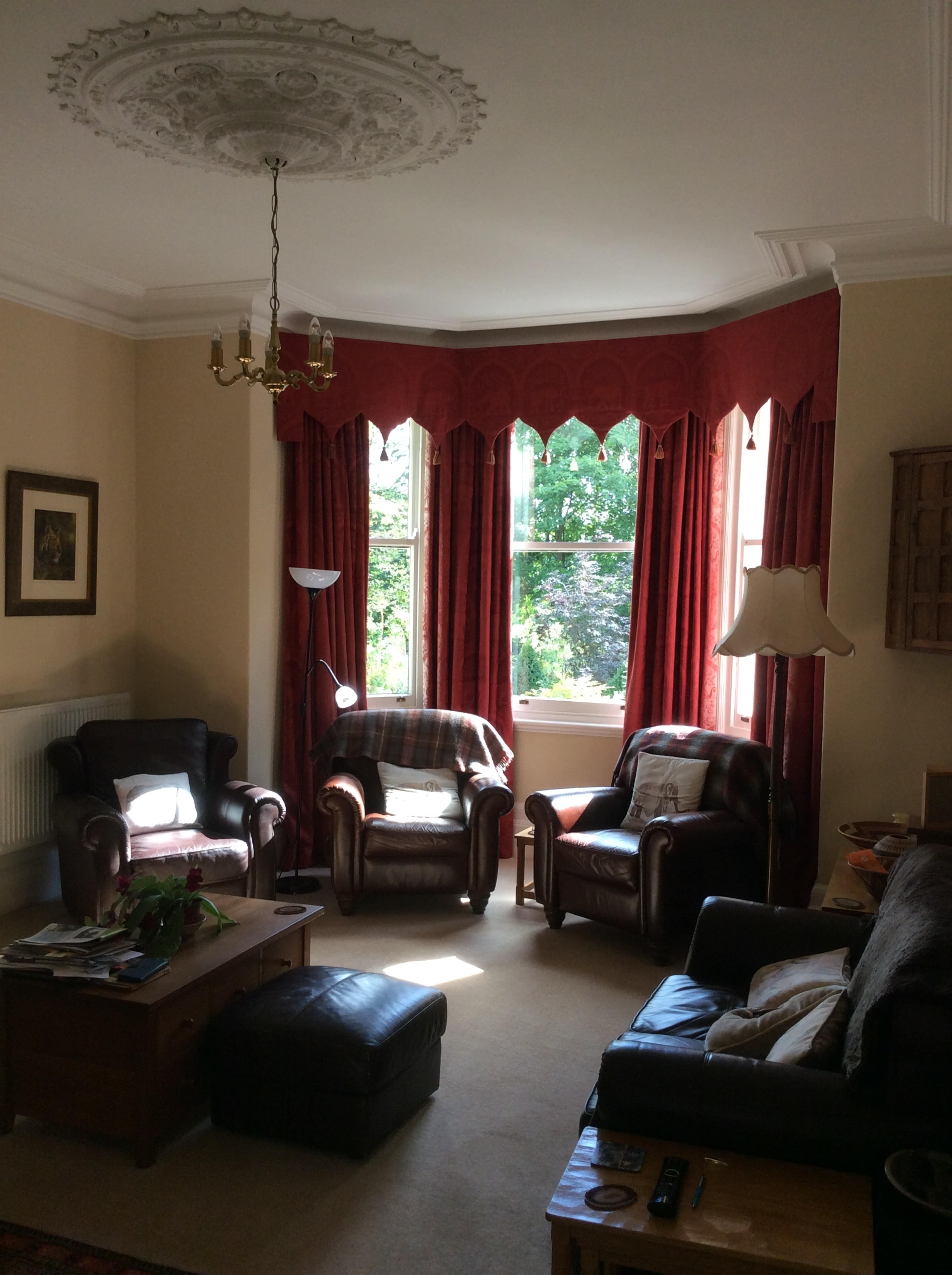 A cozy living room with two leather armchairs, a coffee table, and large windows covered by red curtains.