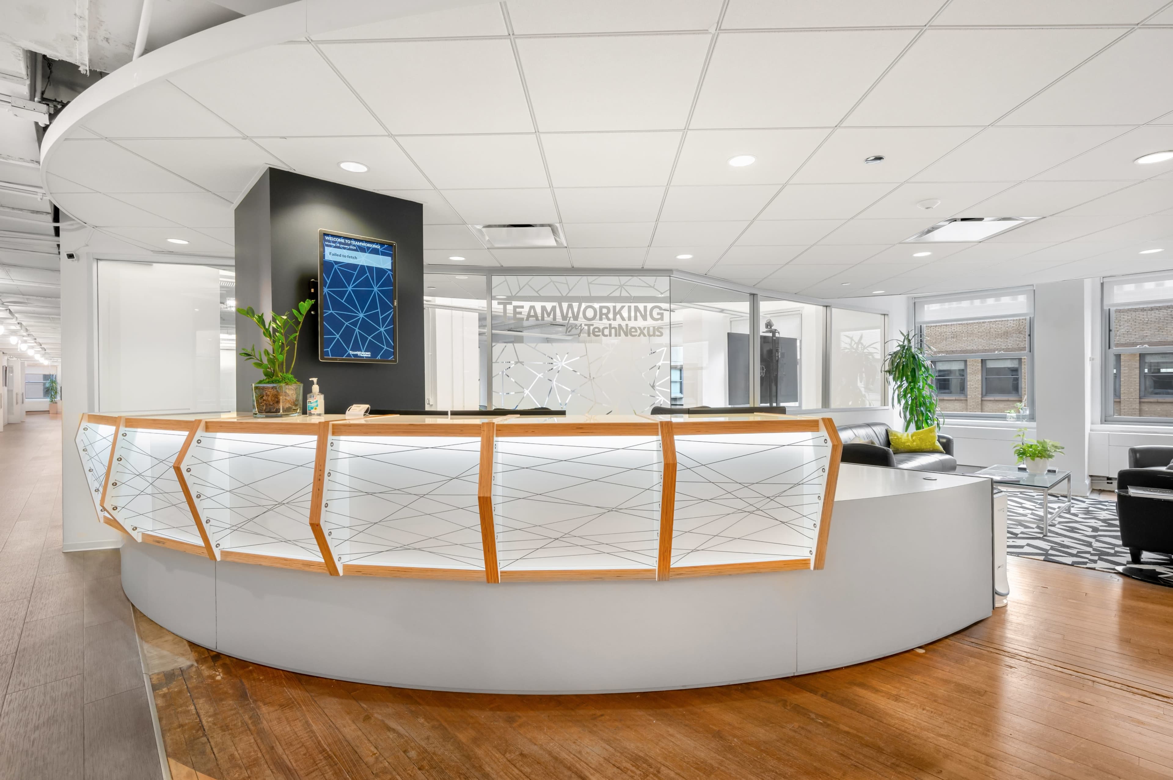 A modern reception area with a curved front desk, a digital display, and seating arrangements in an office environment.
